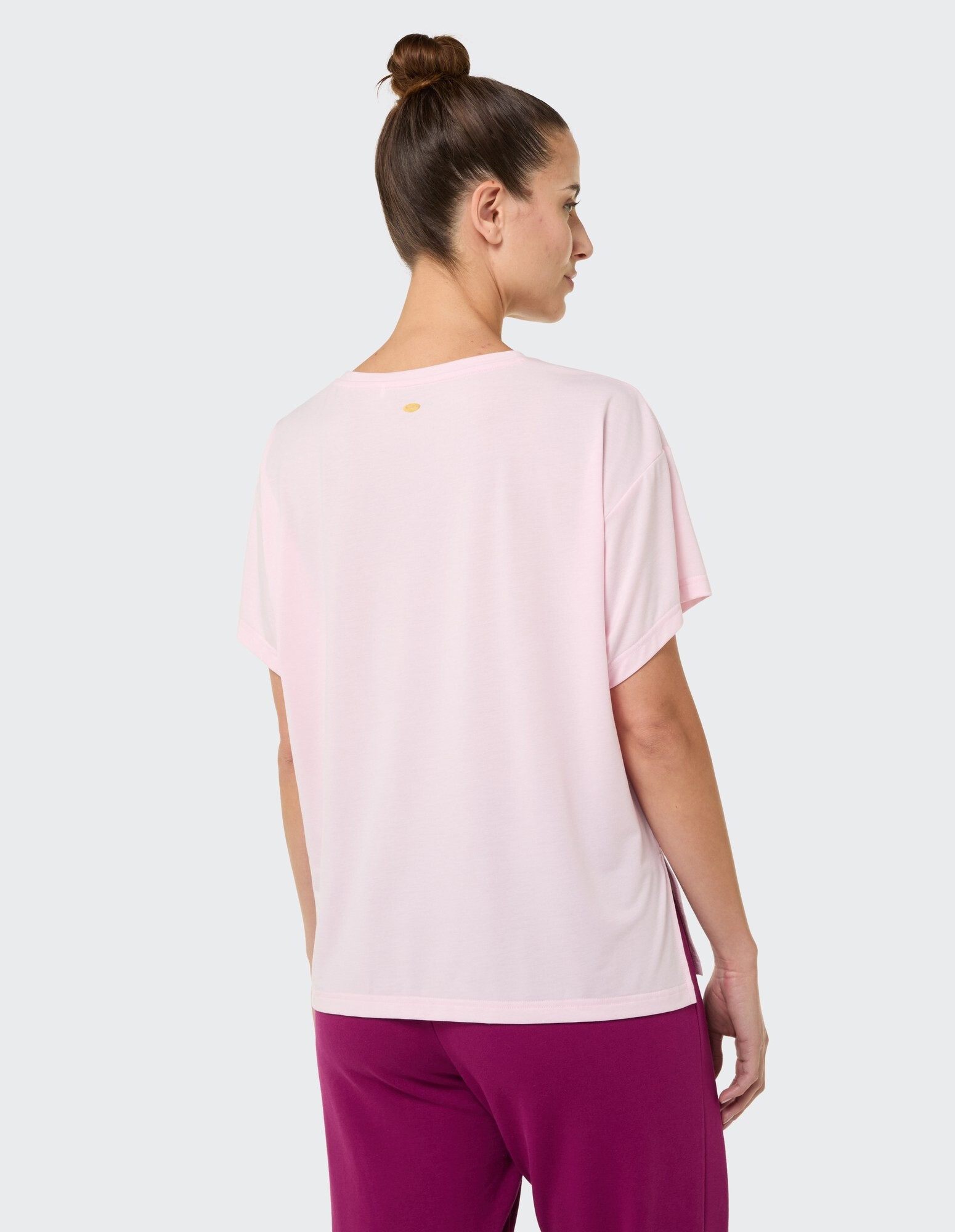 Rückansicht einer Frau in einem rosa Freizeit-T-Shirt und einer lila Hose.