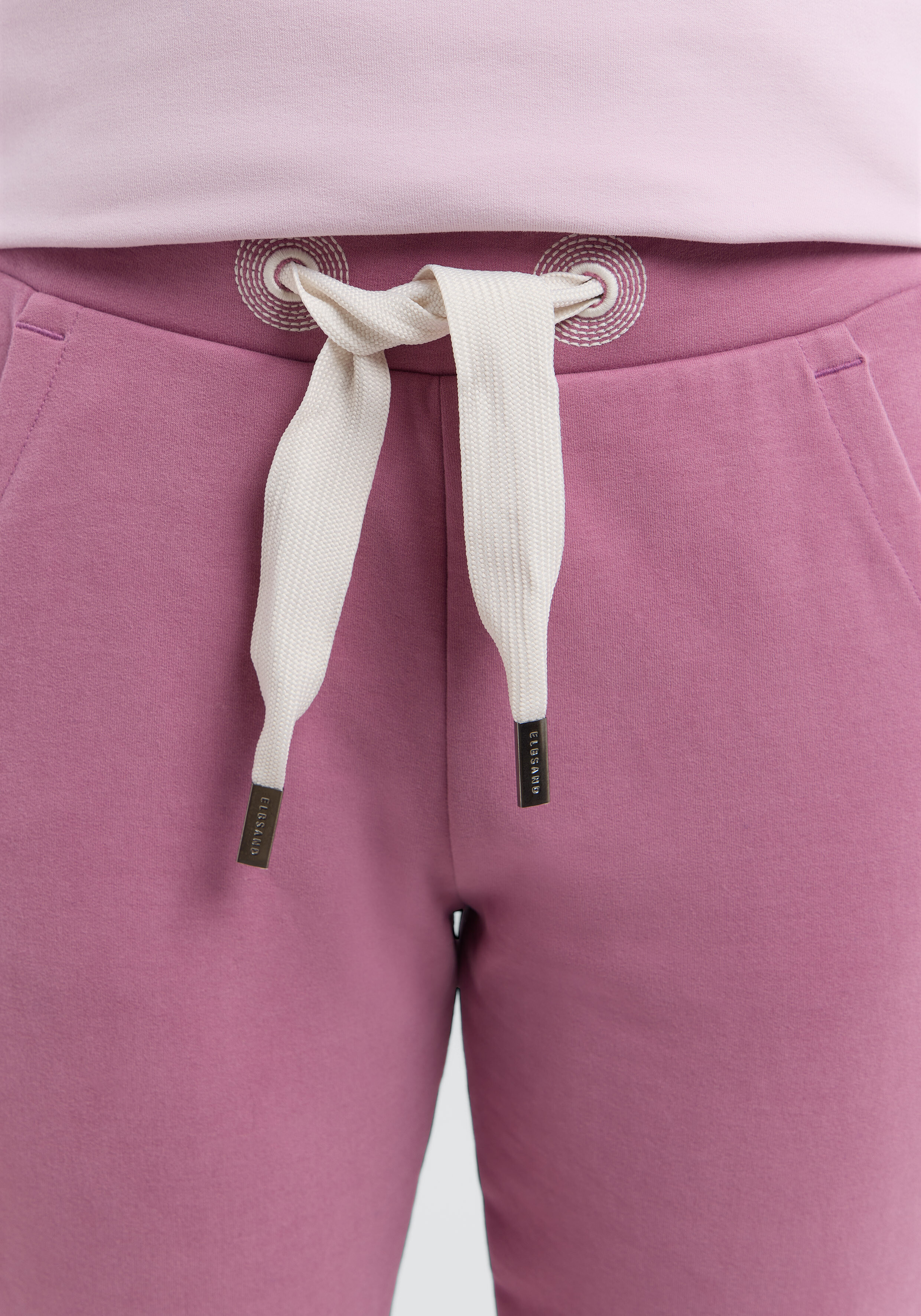 Nahaufnahme einer malvenfarbenen ELBSAND-Jogginghose mit cremefarbenem Kordelzug und metallischen Aglets.