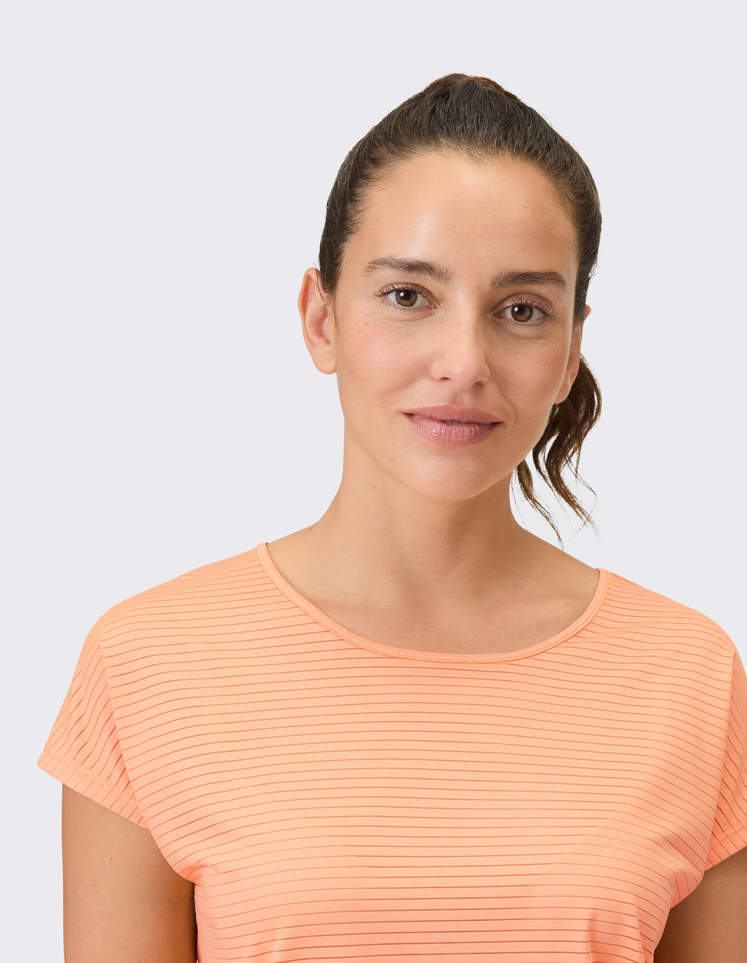Frau trägt ein lässiges, pfirsichfarbenes, gestreiftes T-Shirt für einen bequemen Alltagslook.
