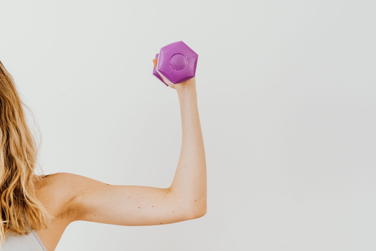 Frau hebt eine lila Hantel und präsentiert lässige Fitnesskleidung und aktiven Lebensstil.