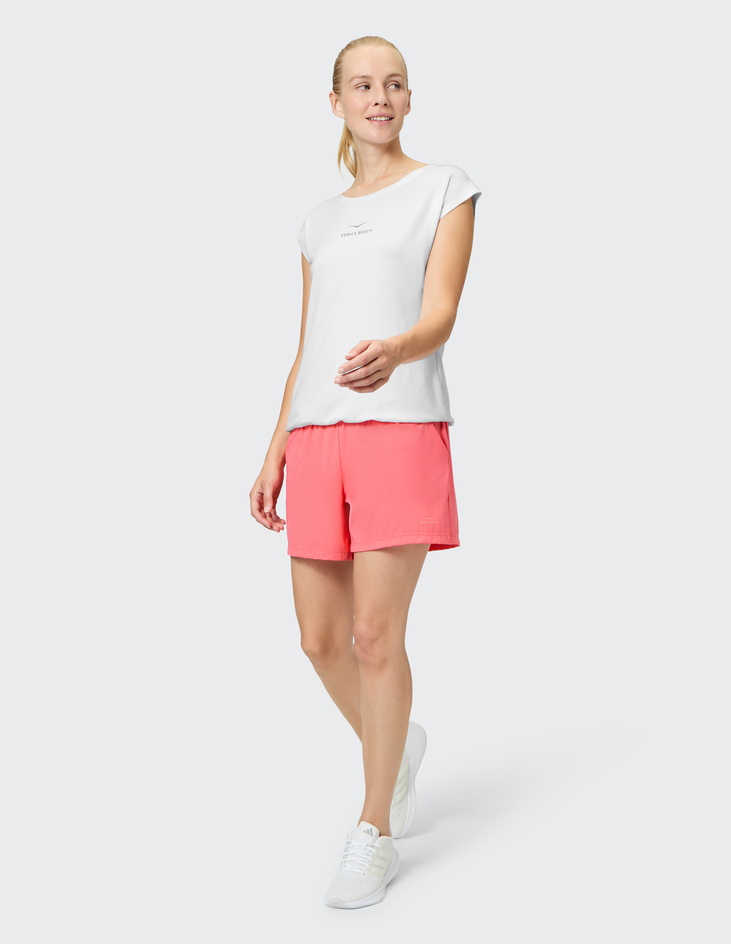 Frau trägt ein weißes T-Shirt und rosa Freizeitshorts für einen bequemen, sportlichen Look.