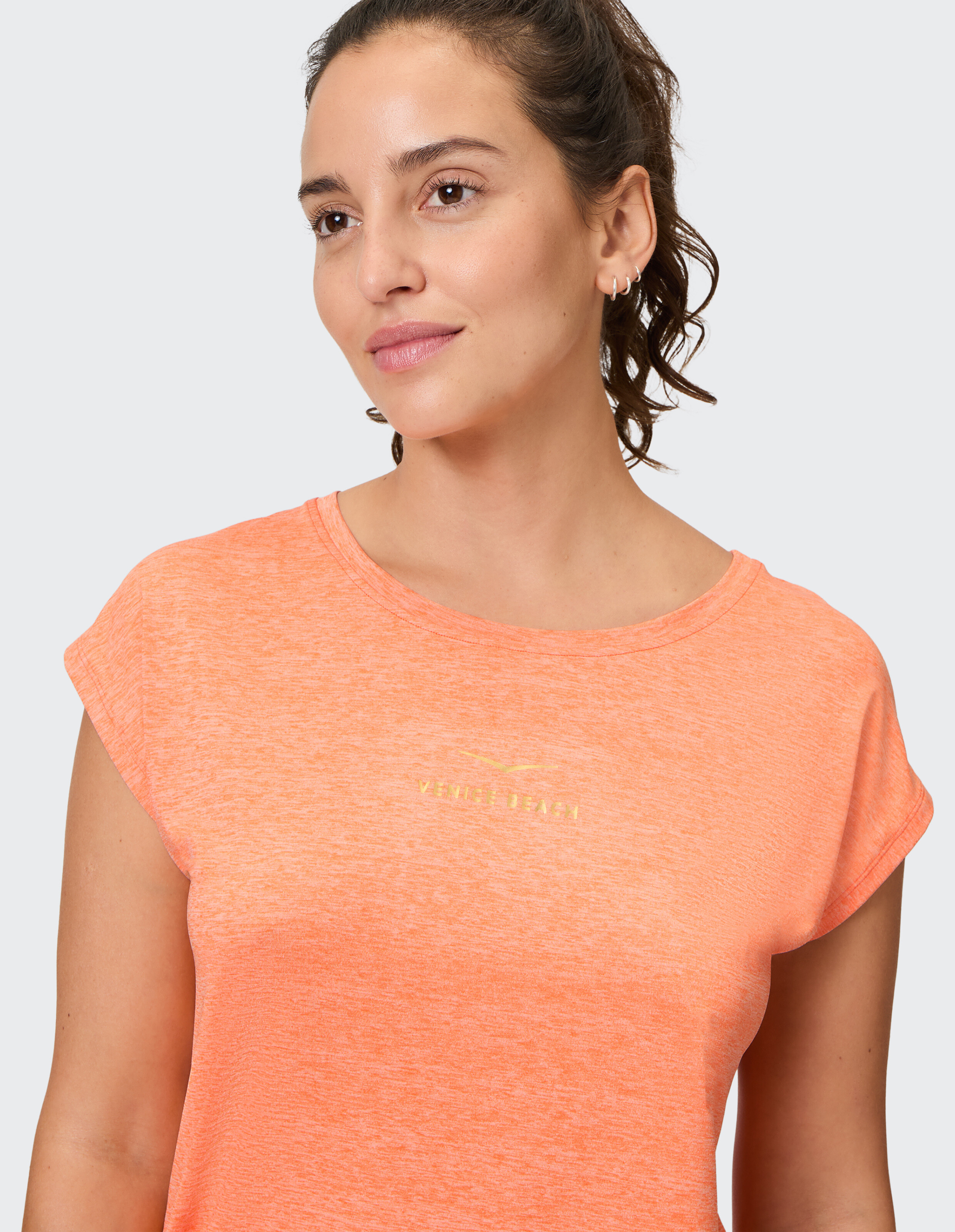 Frau trägt ein gemütliches, orange meliertes Freizeit-T-Shirt mit kleinem Logo.
