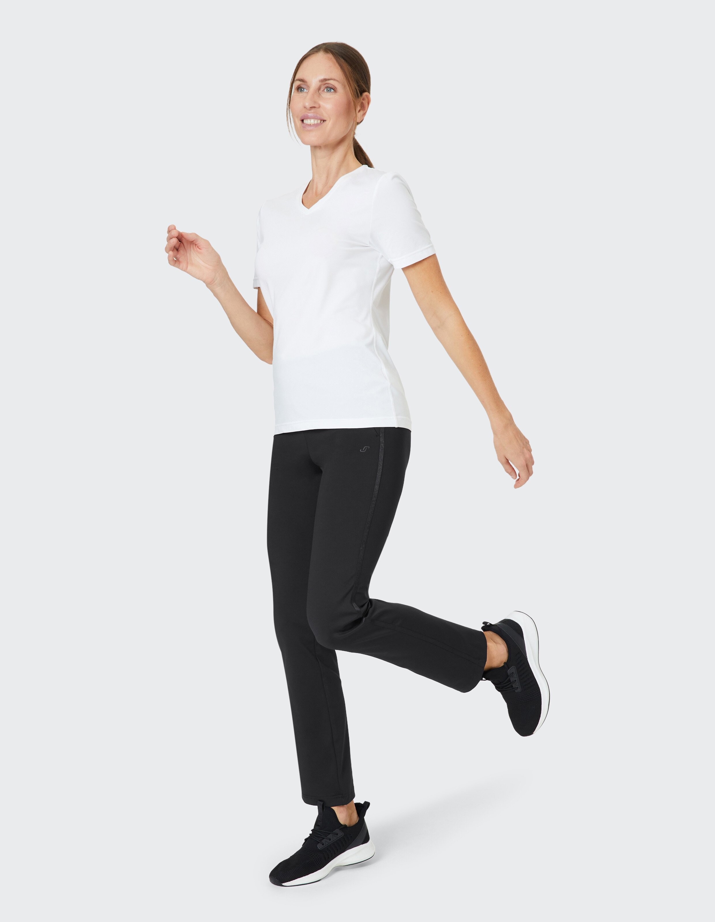 Frau trägt ein weißes T-Shirt mit V-Ausschnitt und eine schwarze Freizeithose für einen bequemen, aktiven Look.