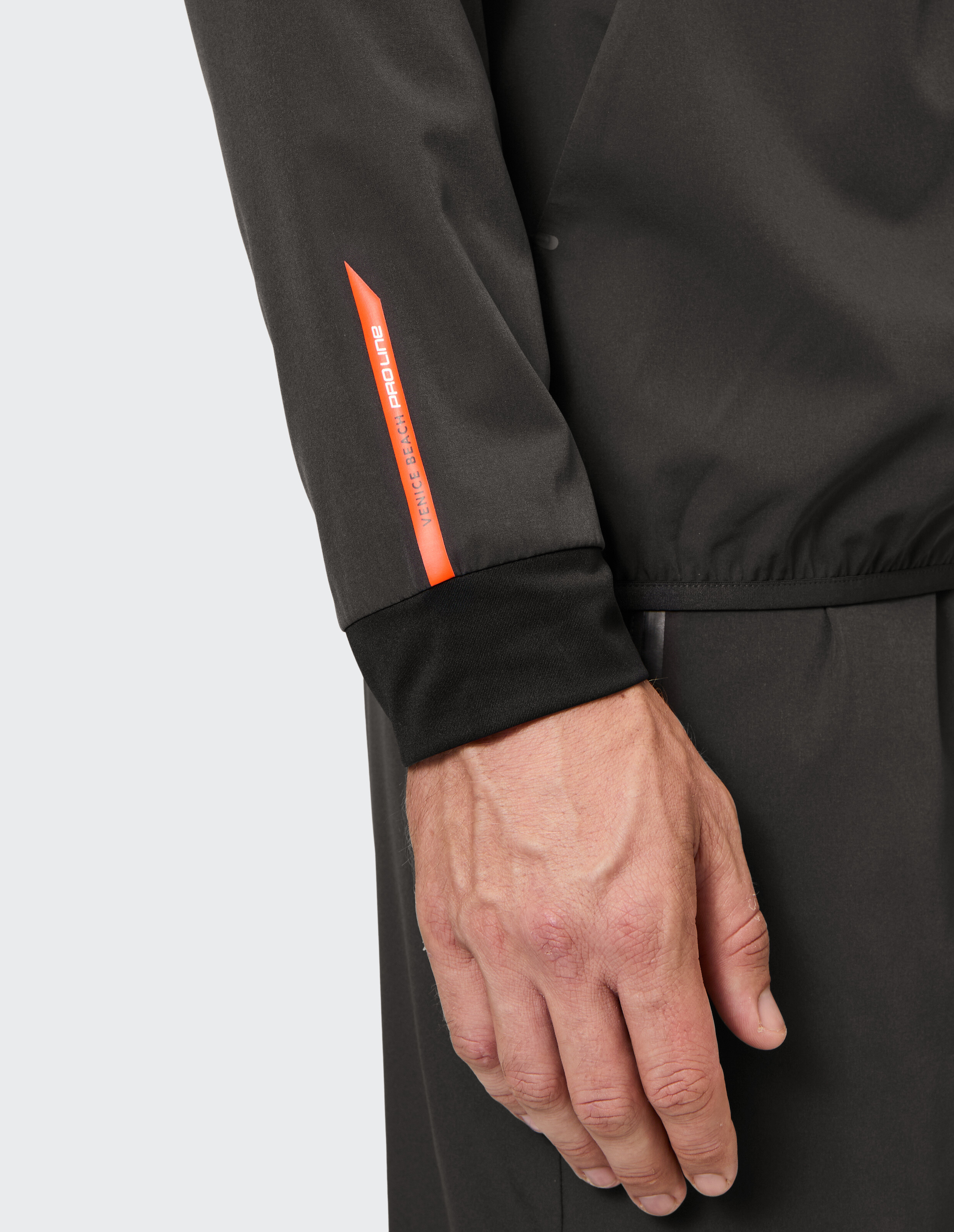 Nahaufnahme eines schwarzen Sportjackenärmels mit orangefarbenem Venice Beach Proline-Branding.