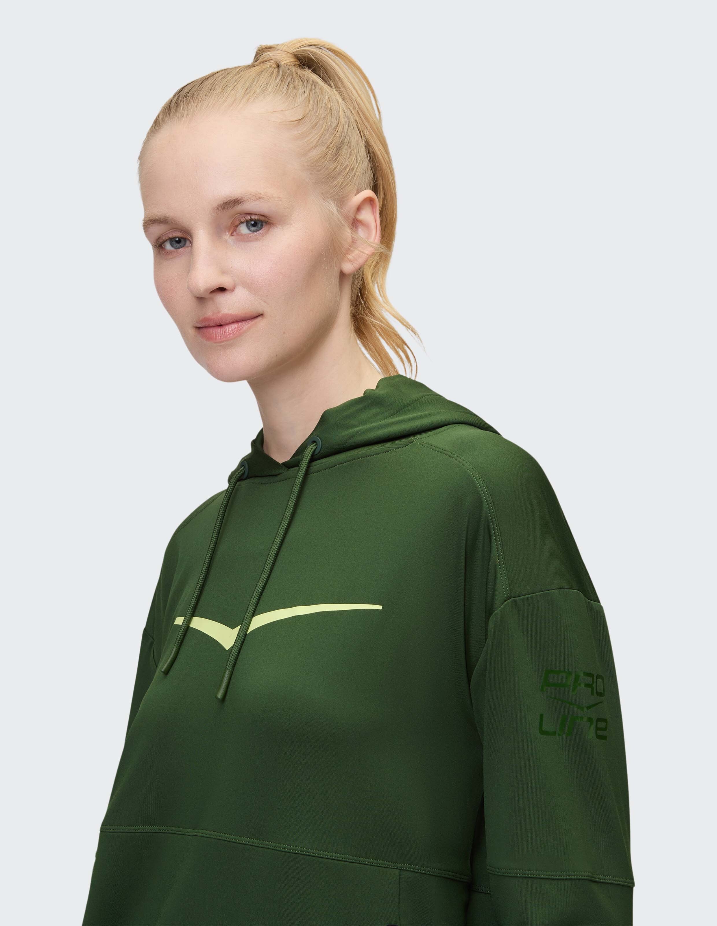 Frau trägt einen dunkelgrünen, lässigen Kapuzenpullover mit lindgrünem Logo und Ärmelaufdruck.