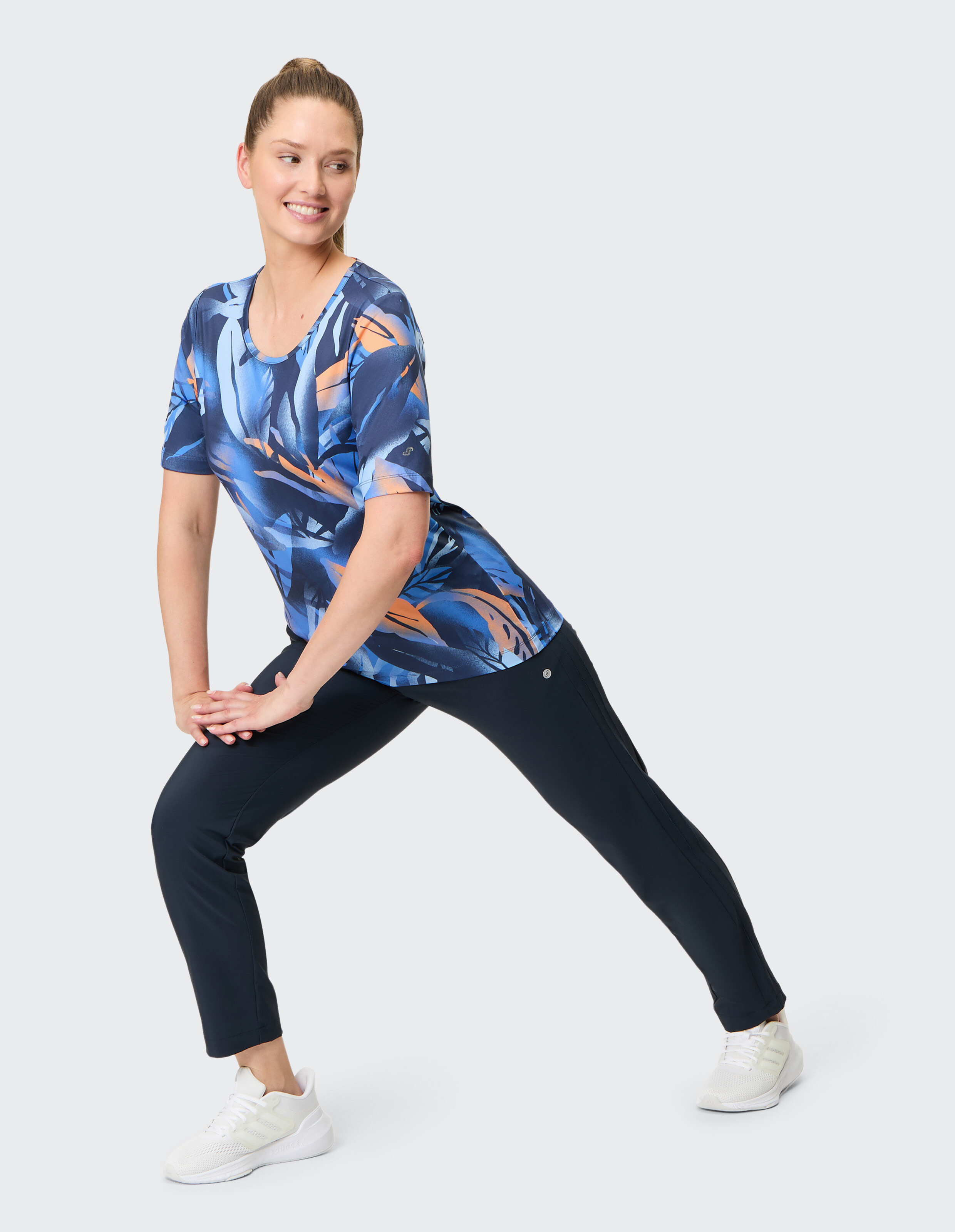 Frau trägt ein blaues T-Shirt mit Blattmuster und dunkle Leggings für lässige Aktivkleidung.