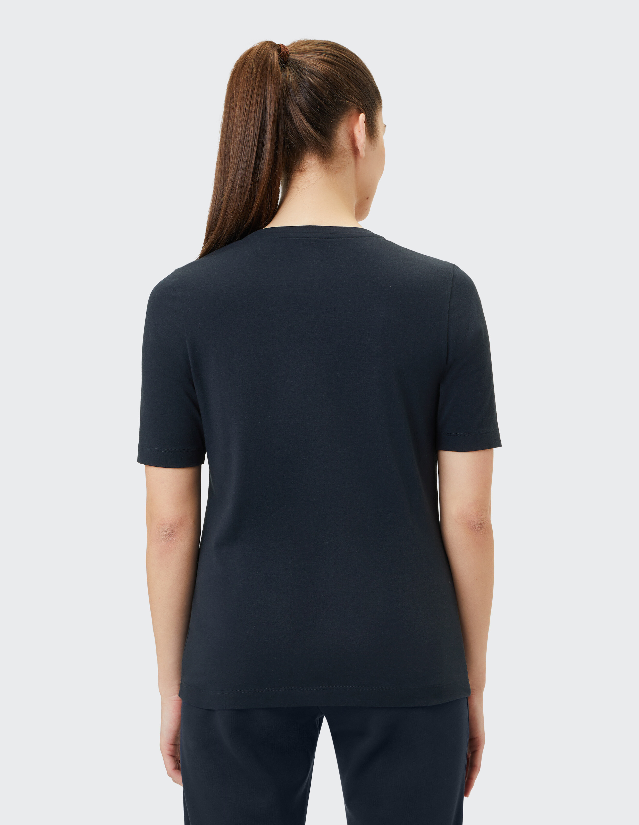 Rückansicht einer Frau, die zum Entspannen ein lässiges dunkelblaues Kurzarm-T-Shirt trägt.