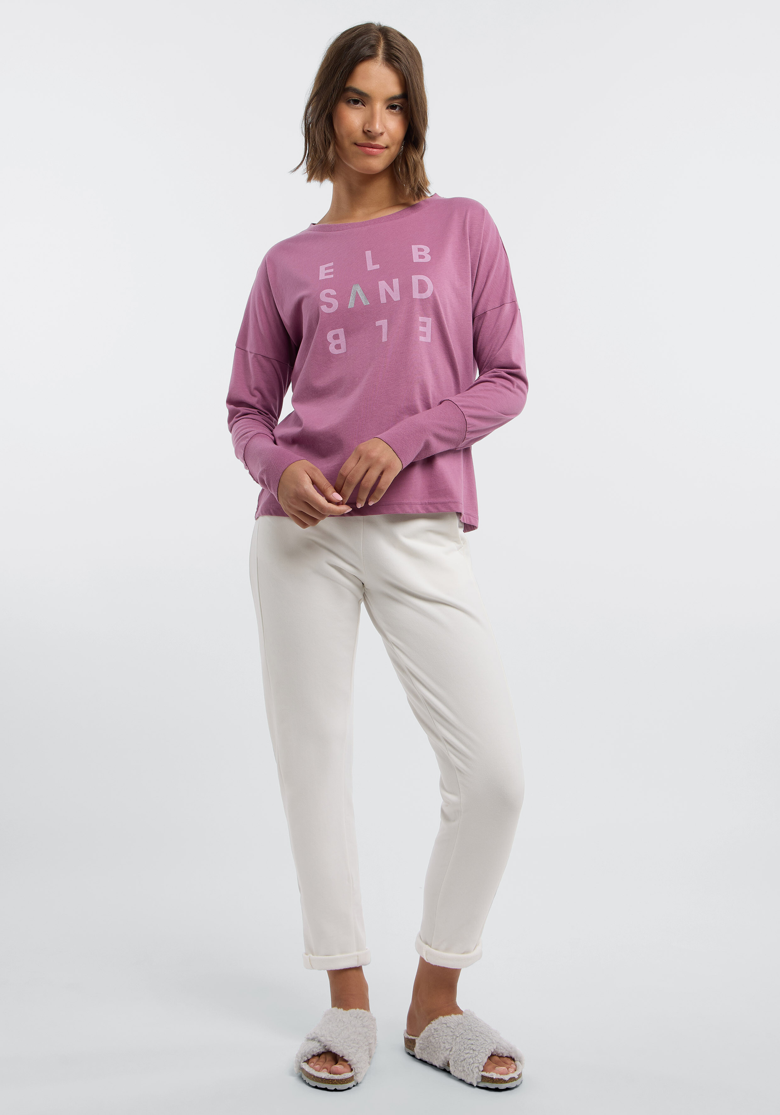 Frau trägt ein lilafarbenes ELBSAND-Langarmshirt und eine weiße Freizeithose.