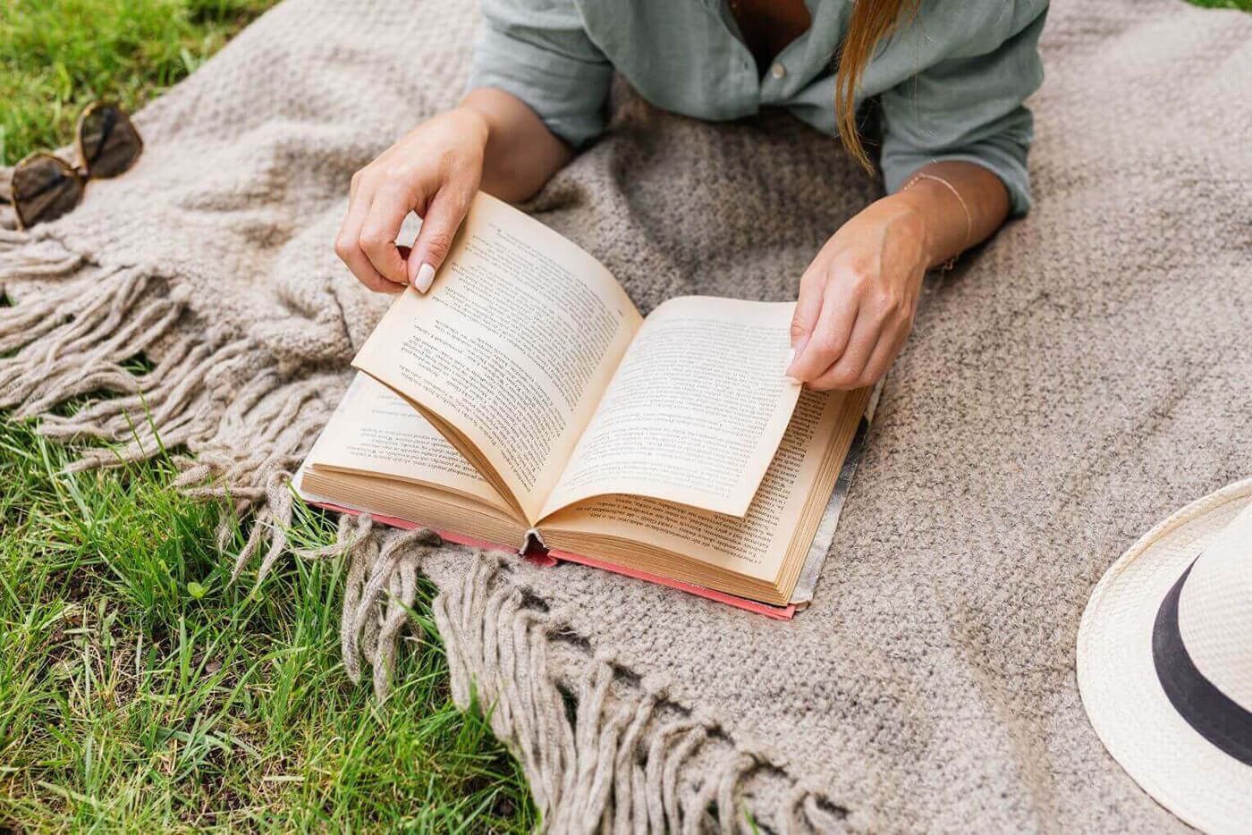 Eine Frau liest auf einer kuscheligen Decke im Gras ein Buch.