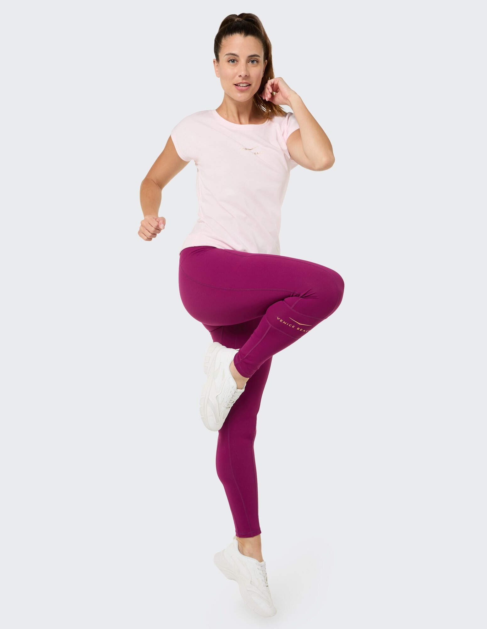 Das Model trägt ein rosa T-Shirt und lila Leggings und präsentiert damit einen lässigen Activewear-Stil.