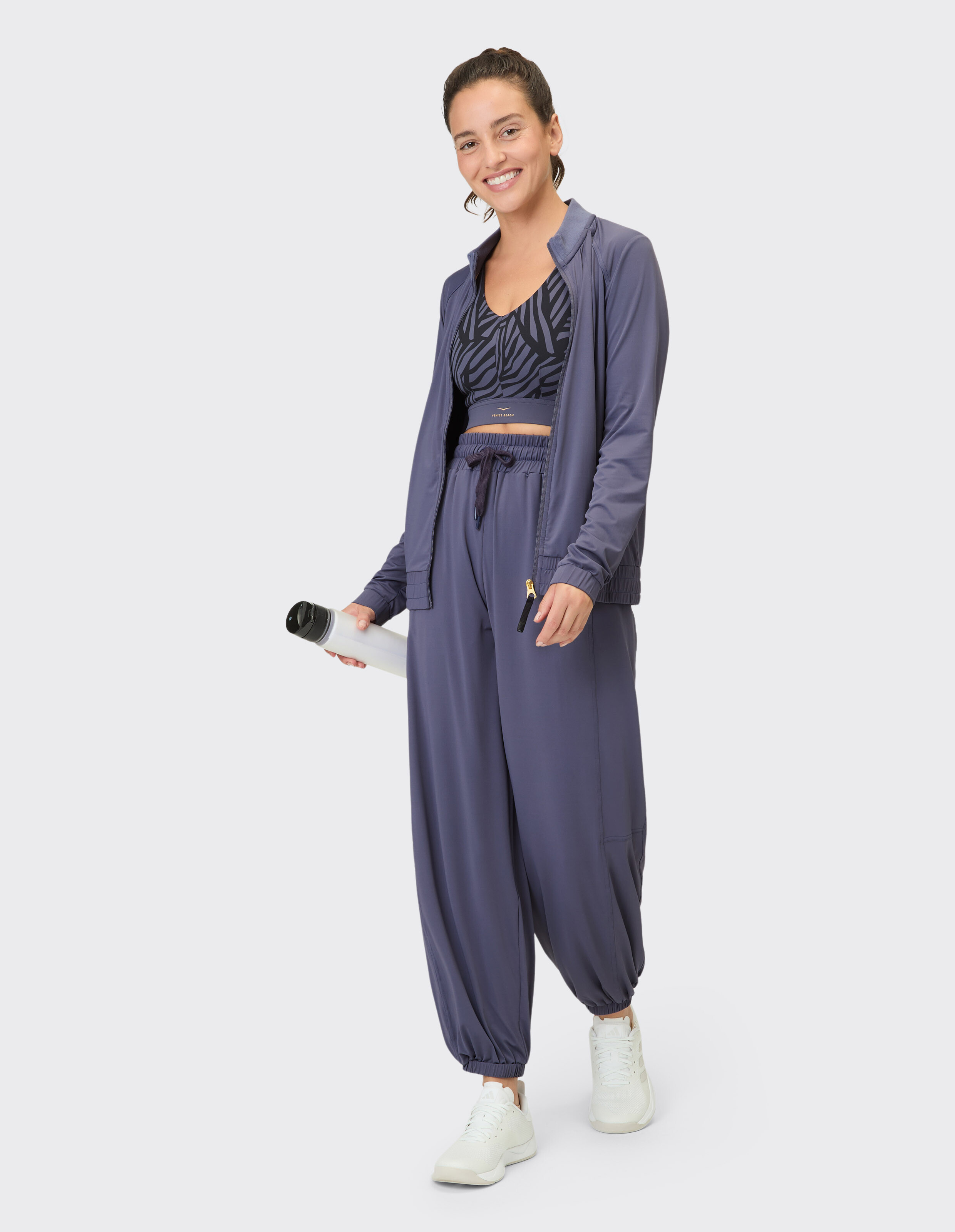 Frau trägt eine blaue ELBSAND-Reißverschlussjacke und Jogginghose mit gemustertem Sport-BH.