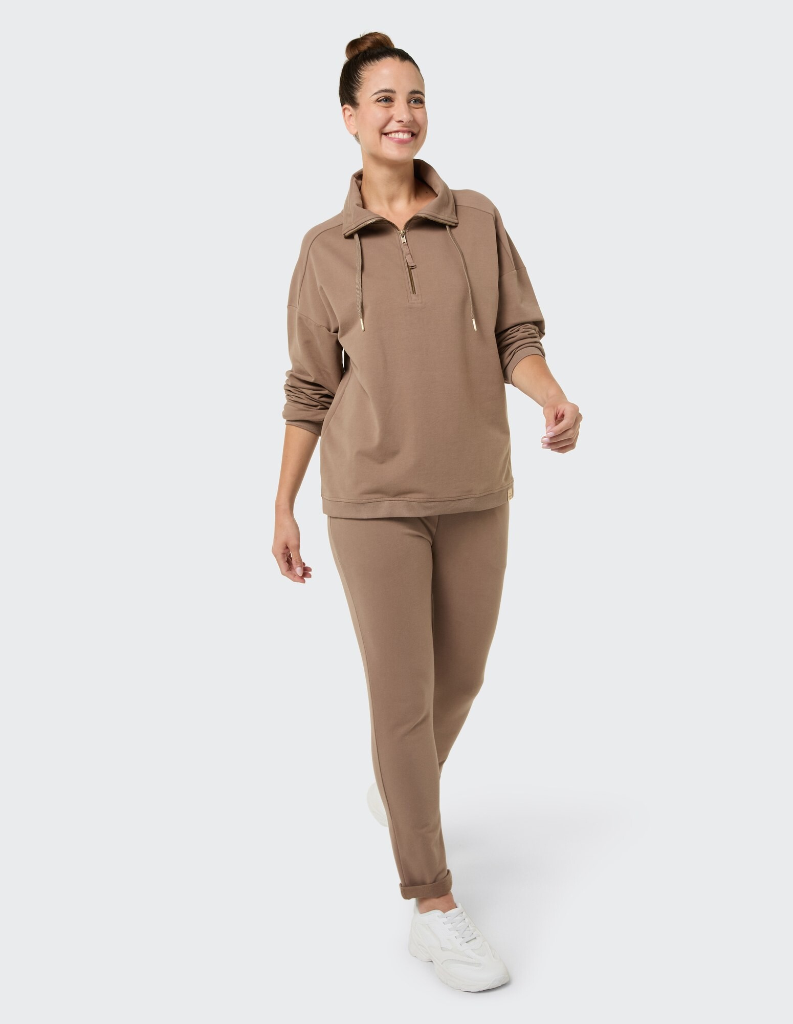 Lächelnde Frau in gemütlichem braunem Sweatshirt mit Reißverschluss und passender Hose, ideal für Freizeitkleidung.