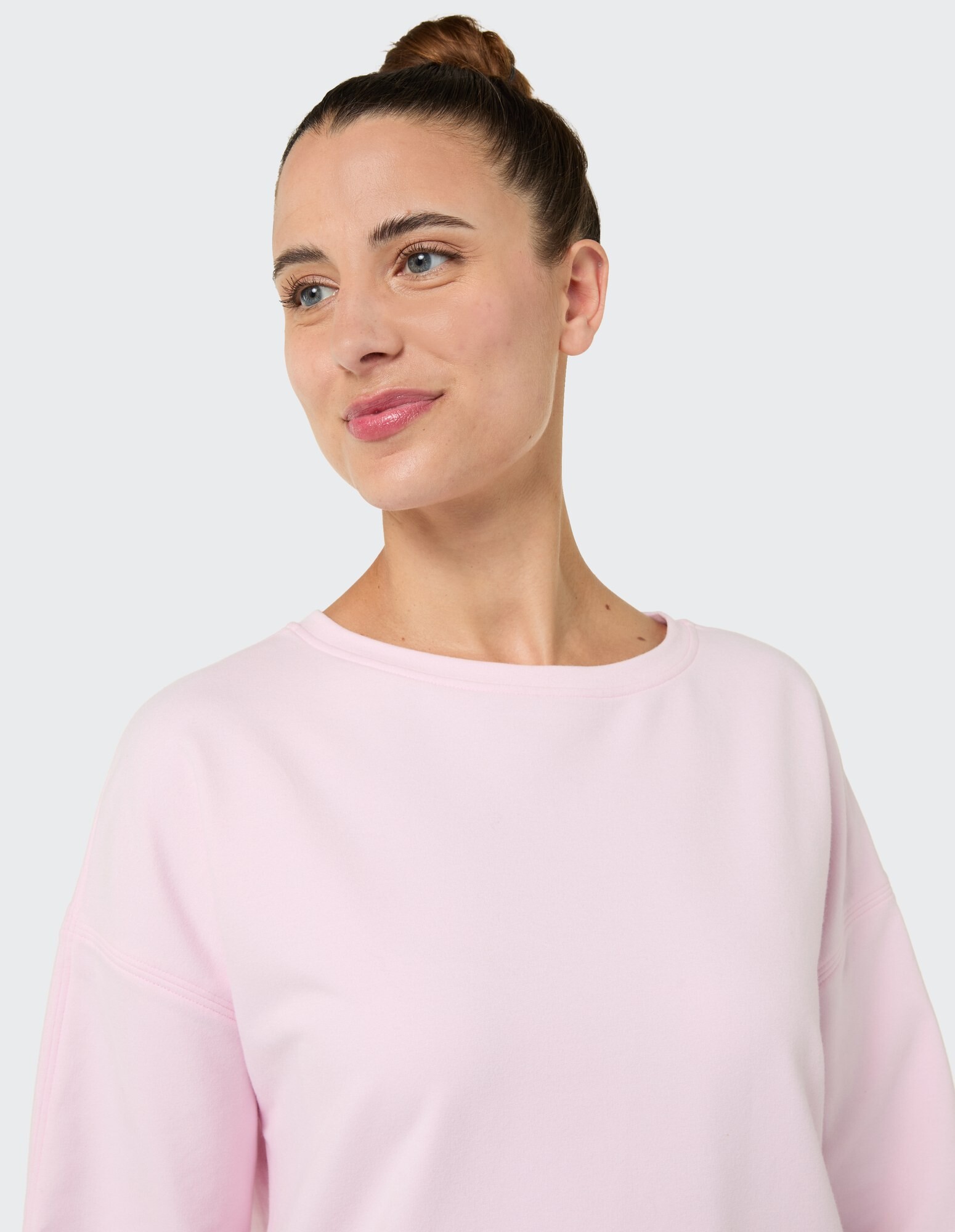 Frau in einem hellrosa Sweatshirt mit lockerer Passform und rundem Ausschnitt.