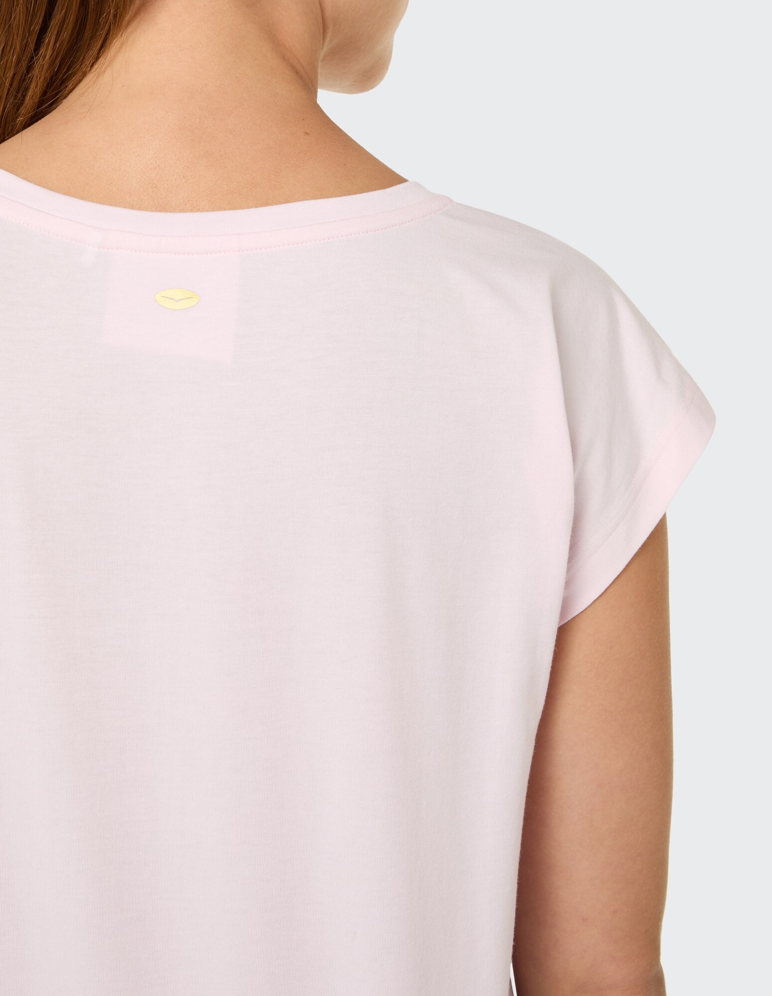 Rückansicht eines zartrosa Freizeit-T-Shirts mit aufgerollten Ärmeln und Logo-Detail.