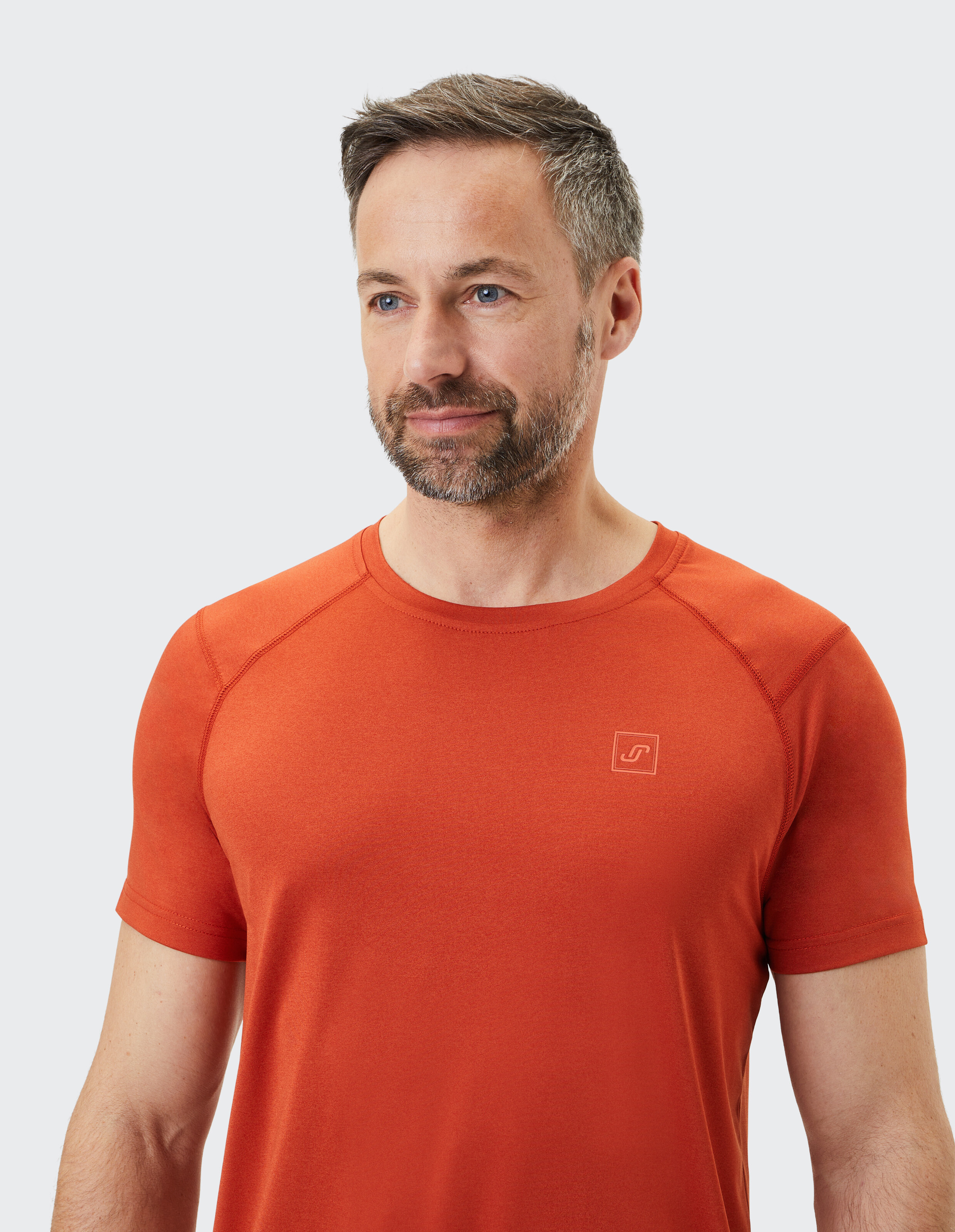 Nahaufnahme eines Mannes, der ein kurzärmliges orangefarbenes T-Shirt mit rundem Ausschnitt und dezentem Logo trägt.