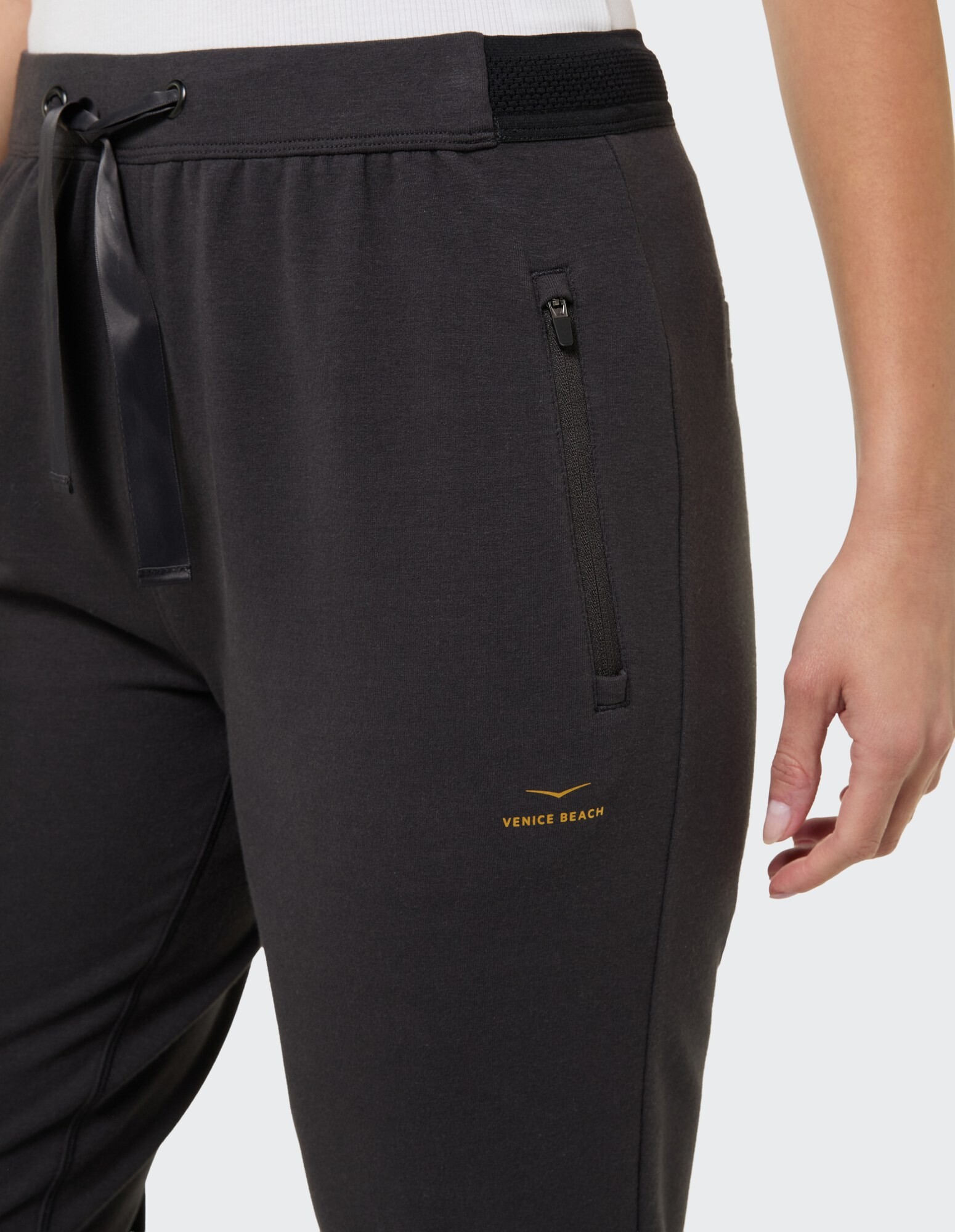 Nahaufnahme einer dunkelgrauen Jogginghose mit elastischem Bund und Venice Beach-Logo.