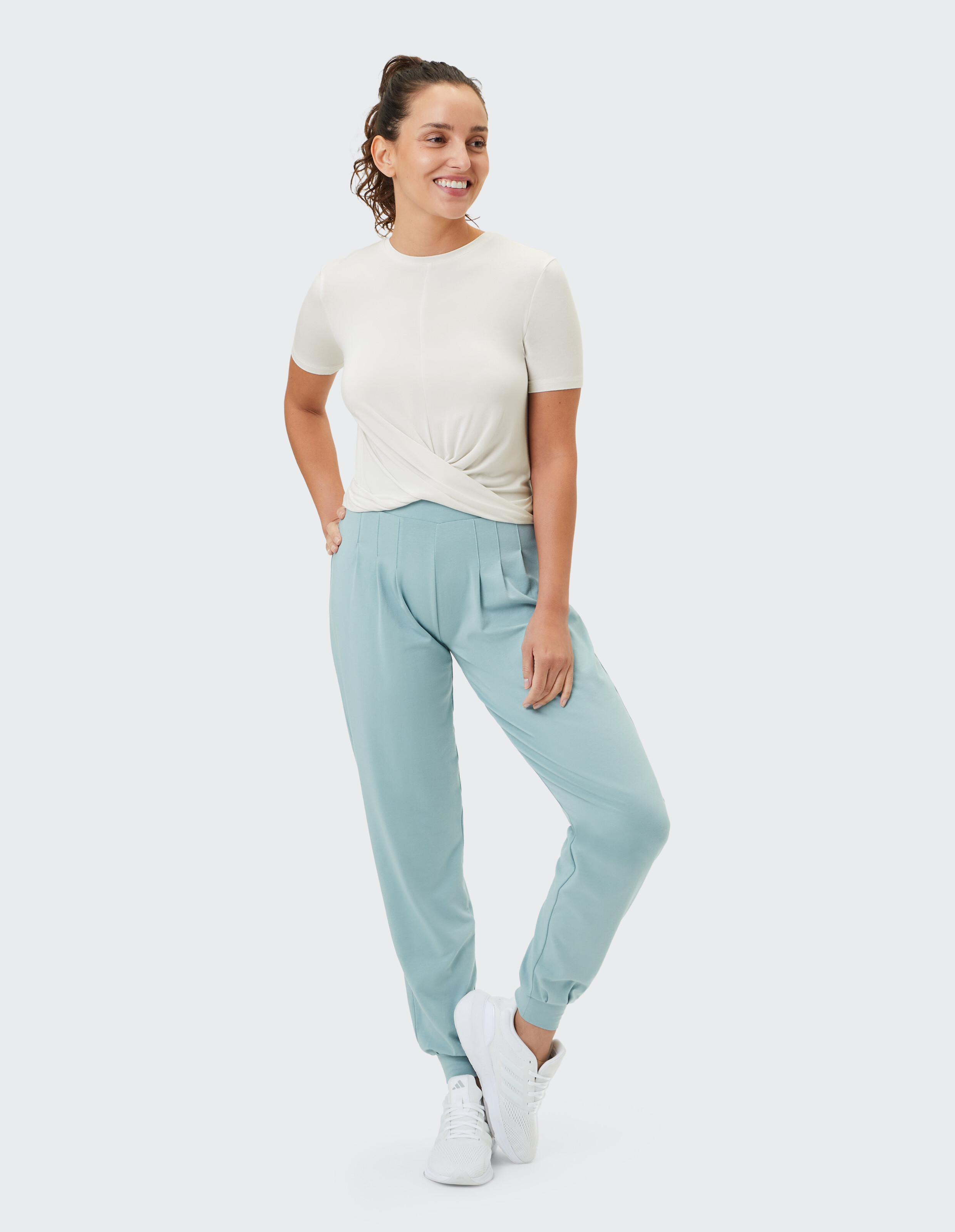 Frau in einem hellcremefarbenen Top und mintgrünen Jogginghosen, lächelnd lässig.