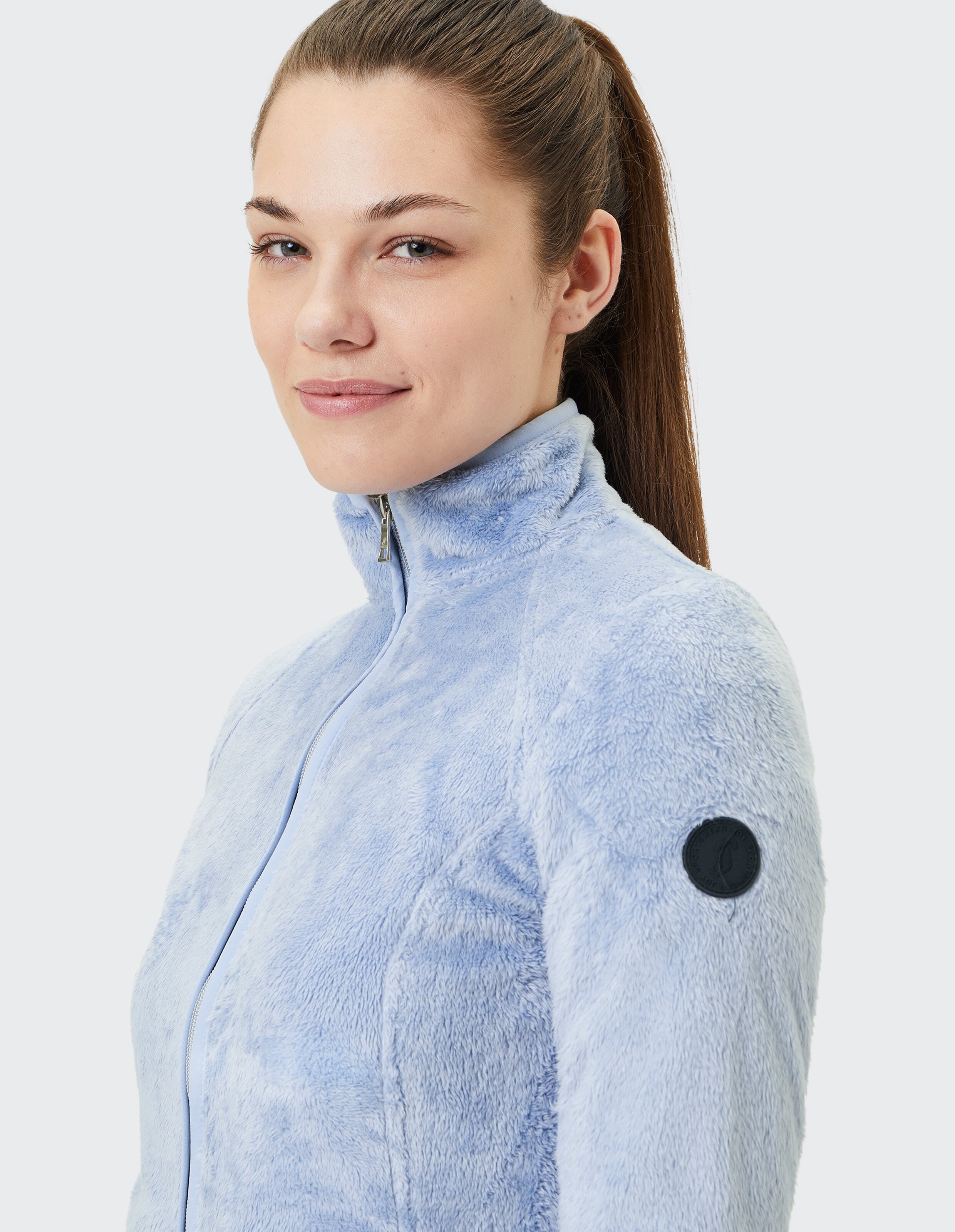Hellblaue, kuschelige Fleecejacke mit hohem Kragen und Logo-Detail.