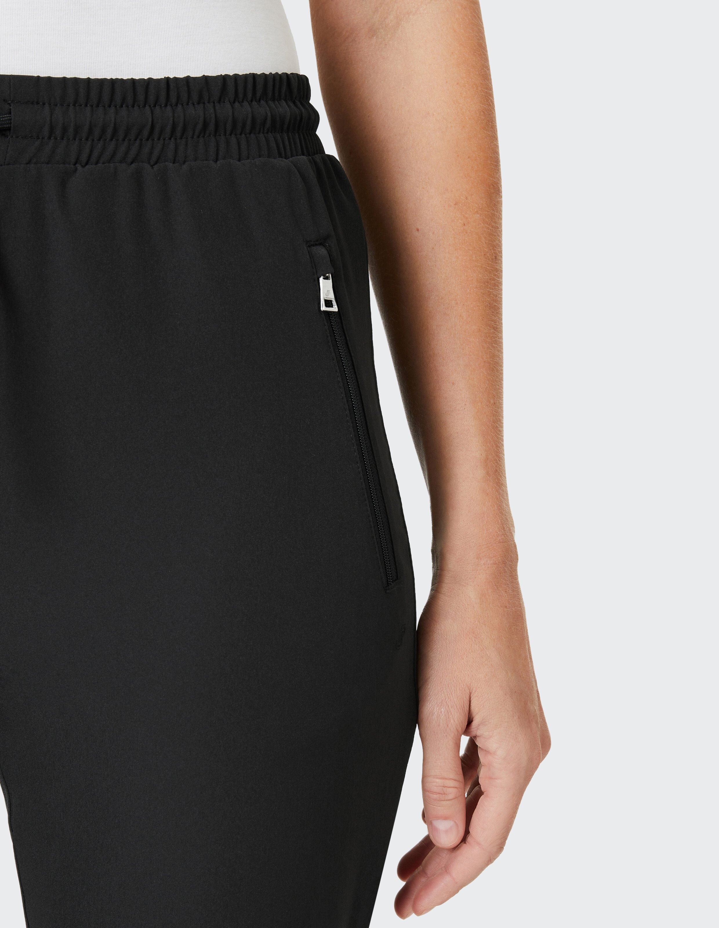 Schwarze Jogginghose mit elastischem Bund, Tunnelzug und seitlichen Reißverschlusstaschen vor weißem Hintergrund.