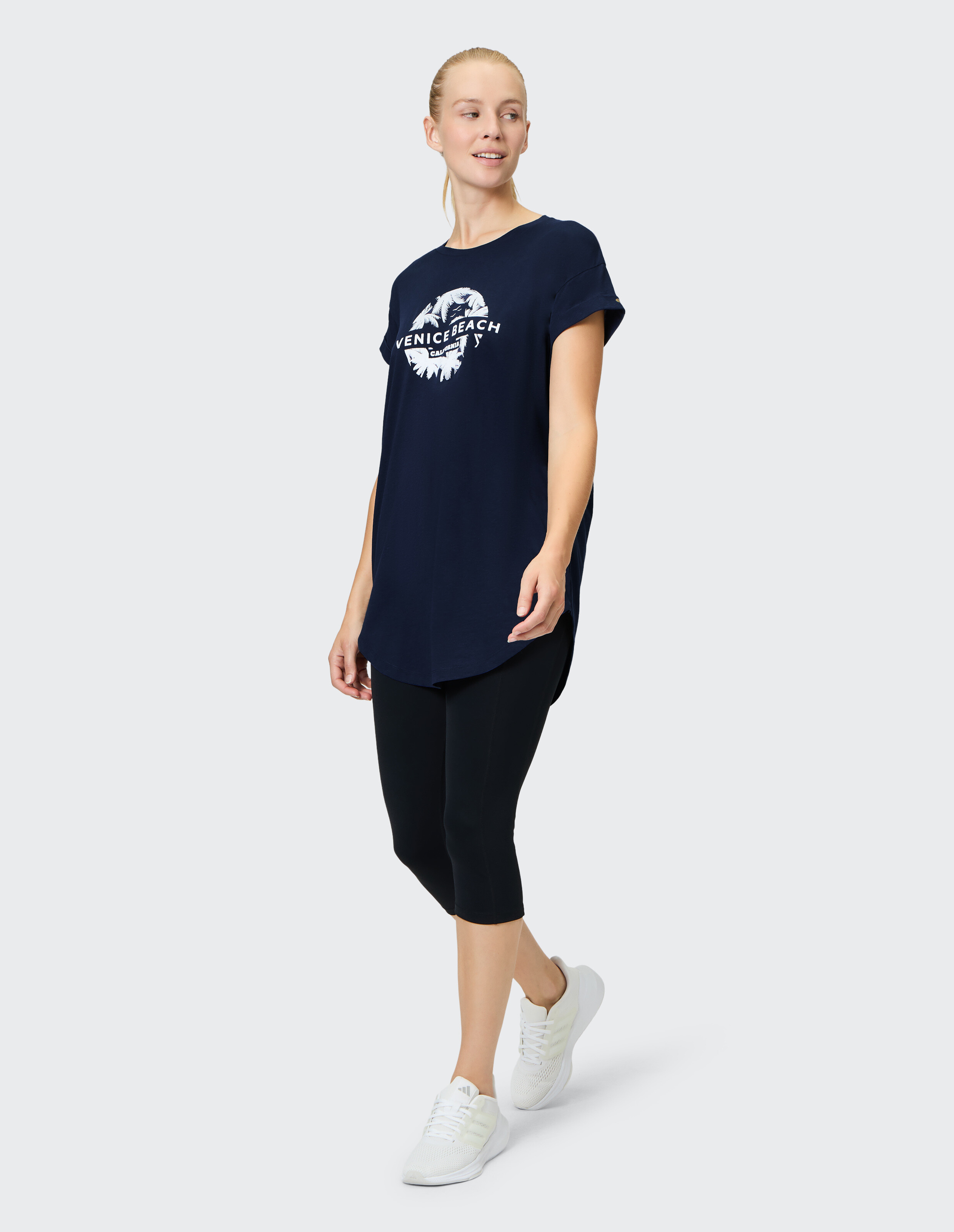 Frau in marineblauem, übergroßem T-Shirt mit „Venice Beach“-Aufdruck und schwarzen Leggings.