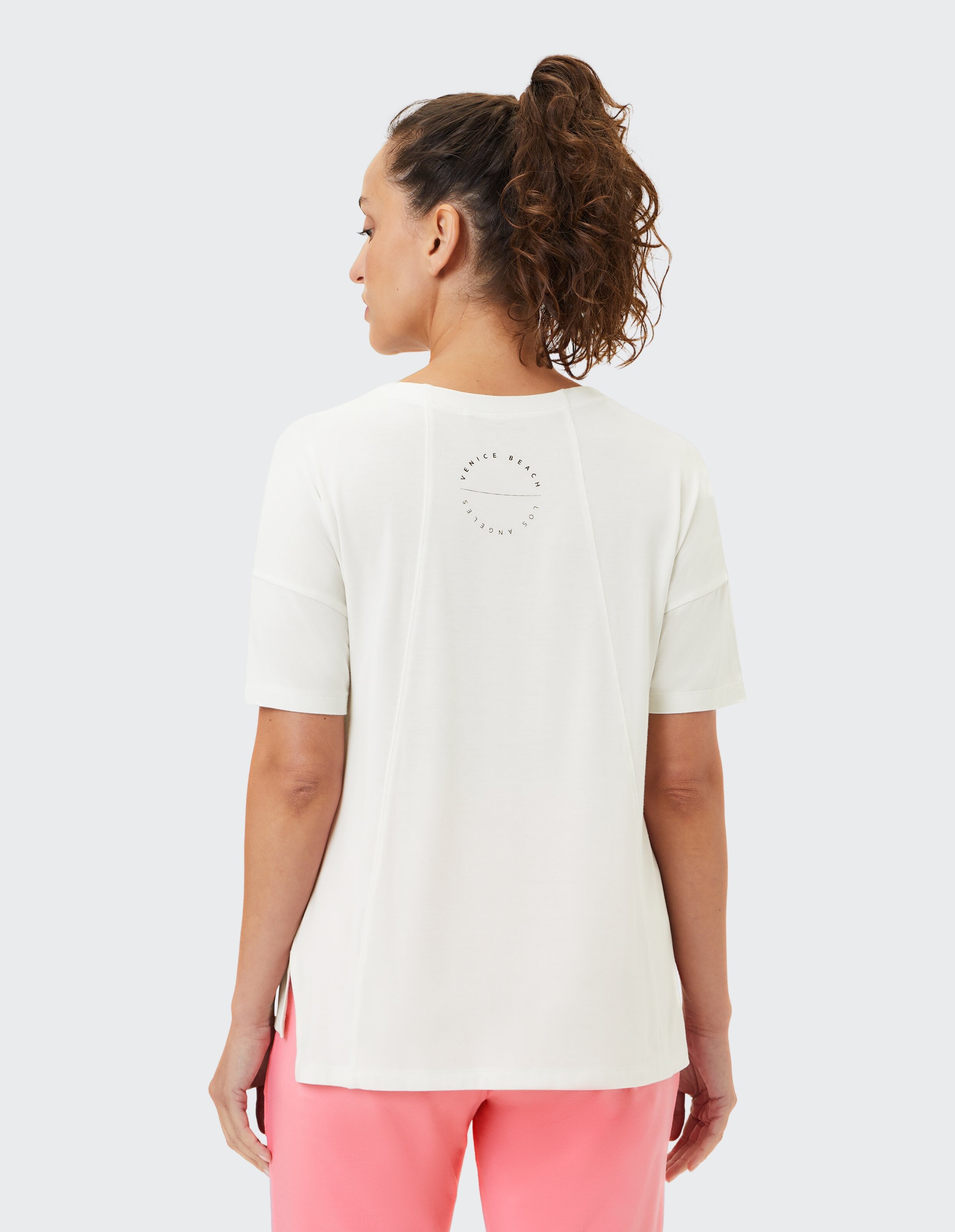 Rückansicht einer Frau in einem weißen Freizeit-T-Shirt mit kurzen Ärmeln.