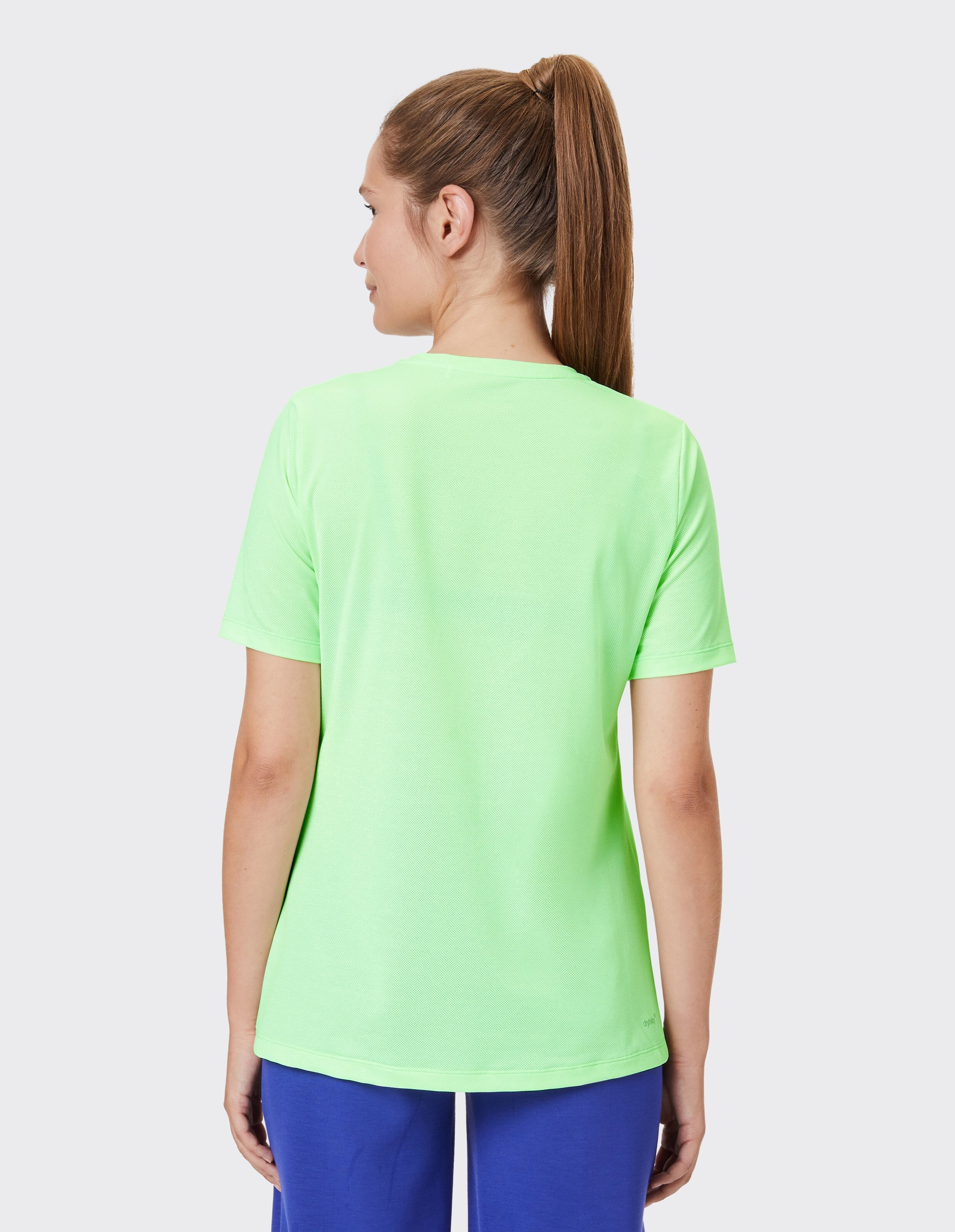 Rückansicht einer Frau in einem hellgrünen Freizeit-T-Shirt und einer blauen Hose.