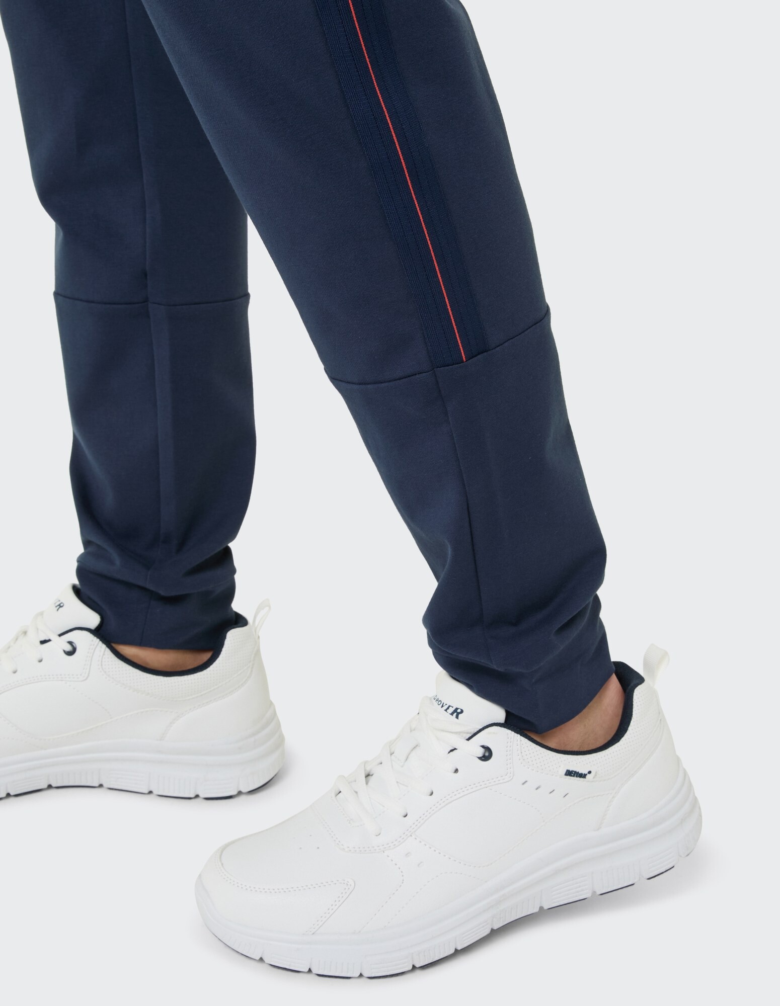 Marineblaue Jogginghosen mit roten Streifen gepaart mit weißen Turnschuhen für Freizeitkleidung.