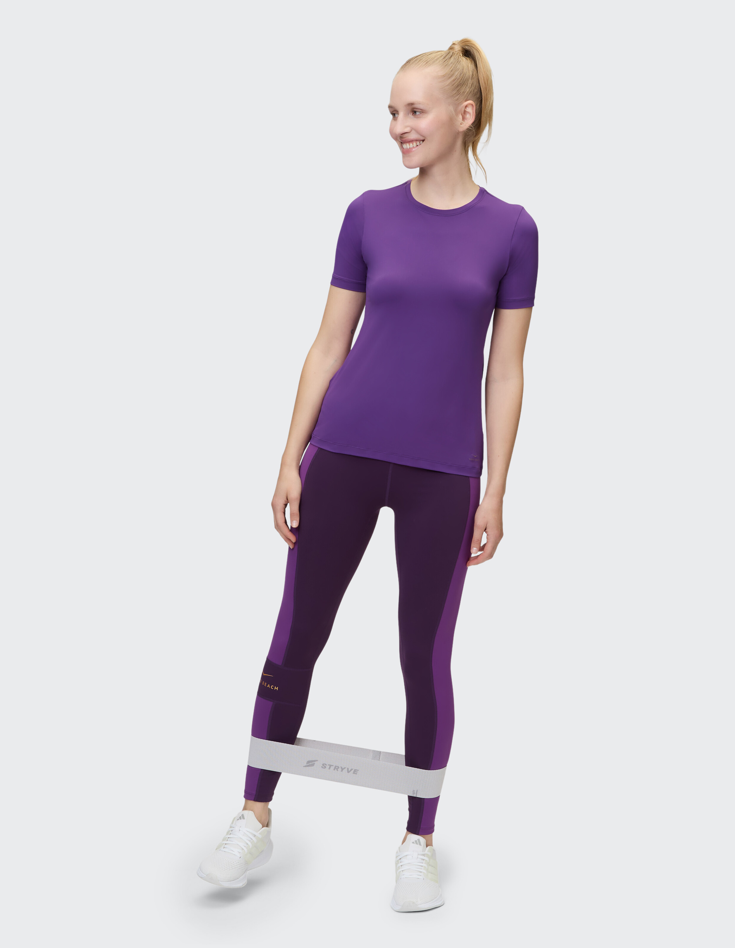 Frau in lila Sportbekleidung und Leggings nutzt ein Widerstandsband für Fitness.