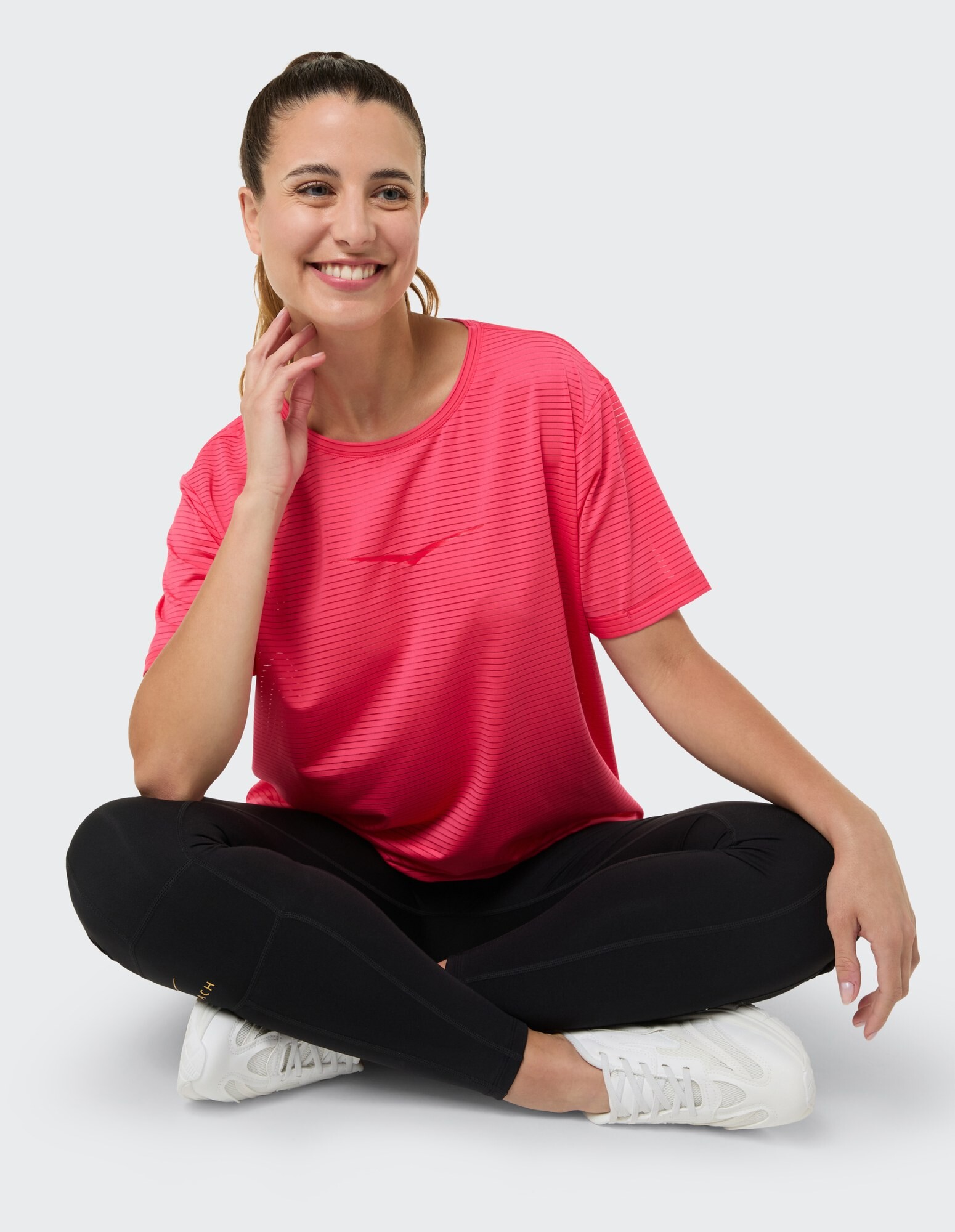 Lächelnde Frau in rosa gestreiftem T-Shirt und schwarzen Leggings sitzt bequem.