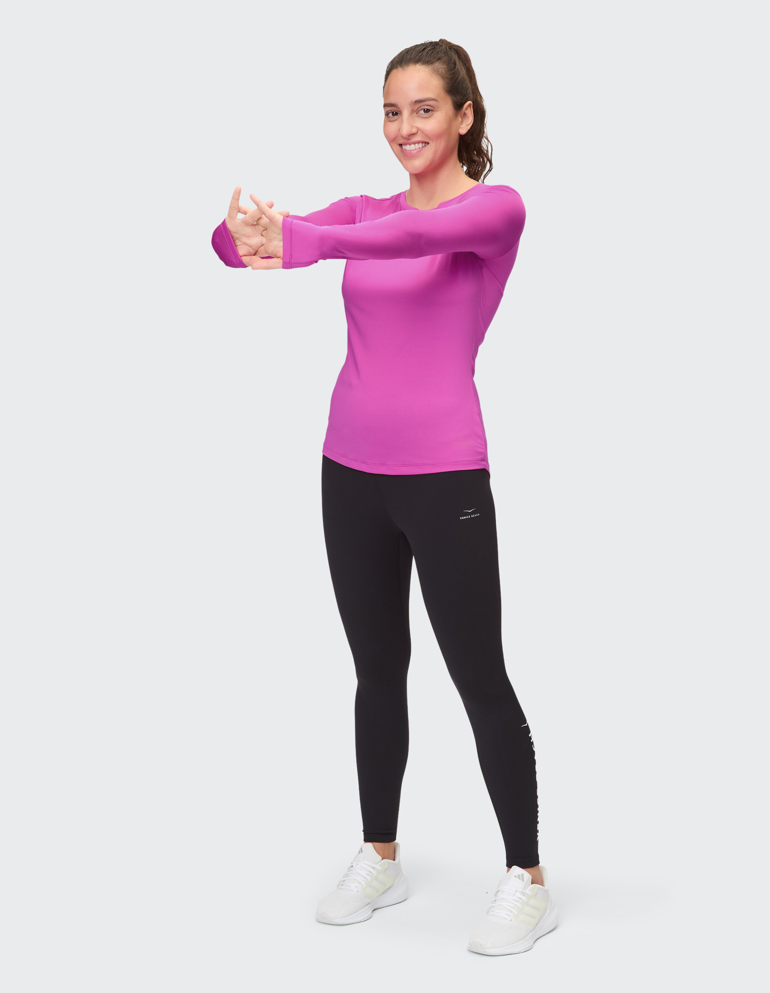 Frau in einem rosafarbenen Langarmshirt und schwarzen Leggings beim Stretching für ein lässiges Training.