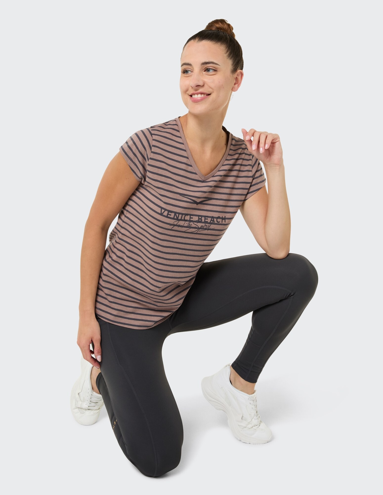 Frau in gestreiftem T-Shirt mit V-Ausschnitt und schwarzen Leggings posiert bequem.