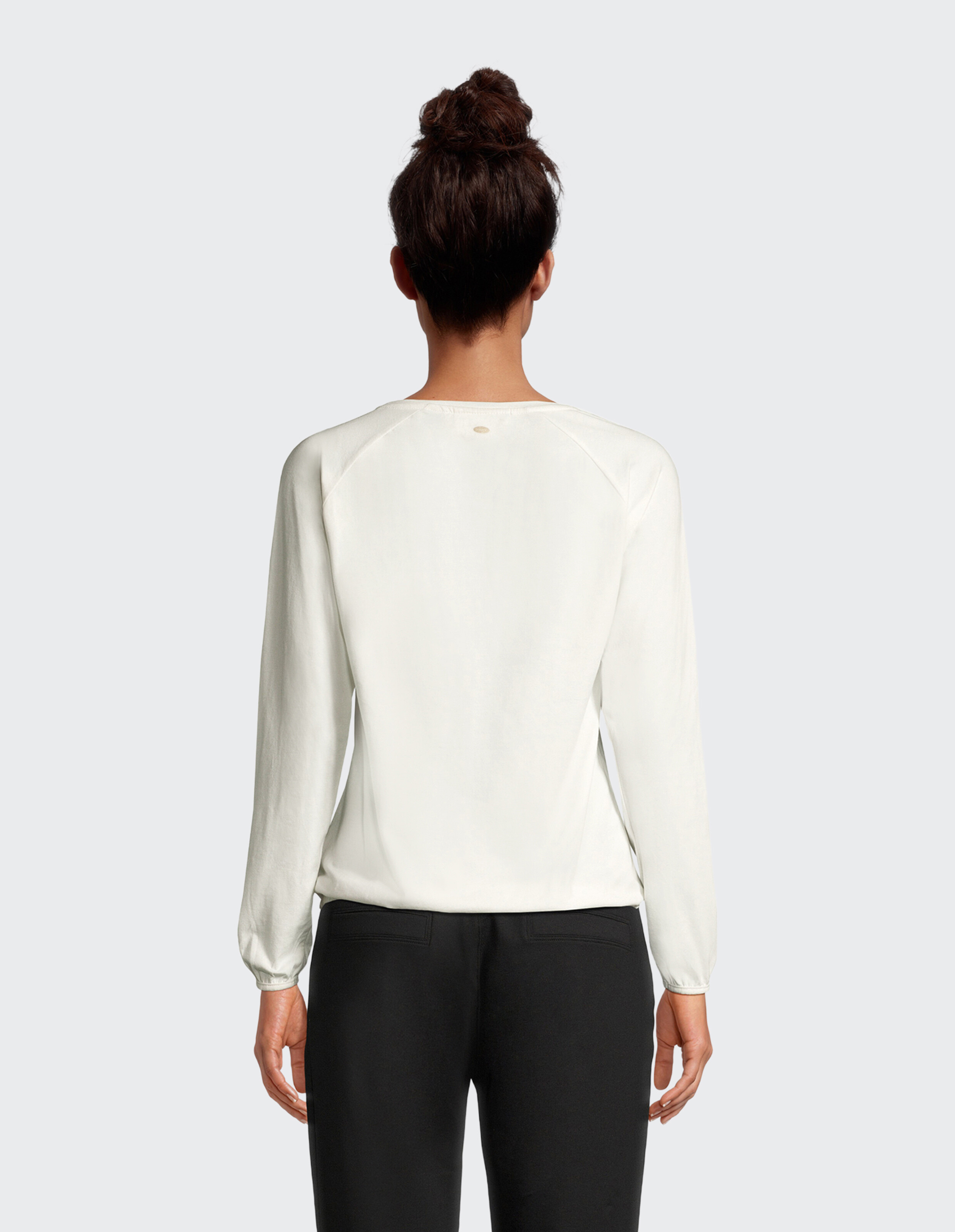 Rückansicht einer Frau in einem hellcremefarbenen Langarmshirt und einer schwarzen Hose.