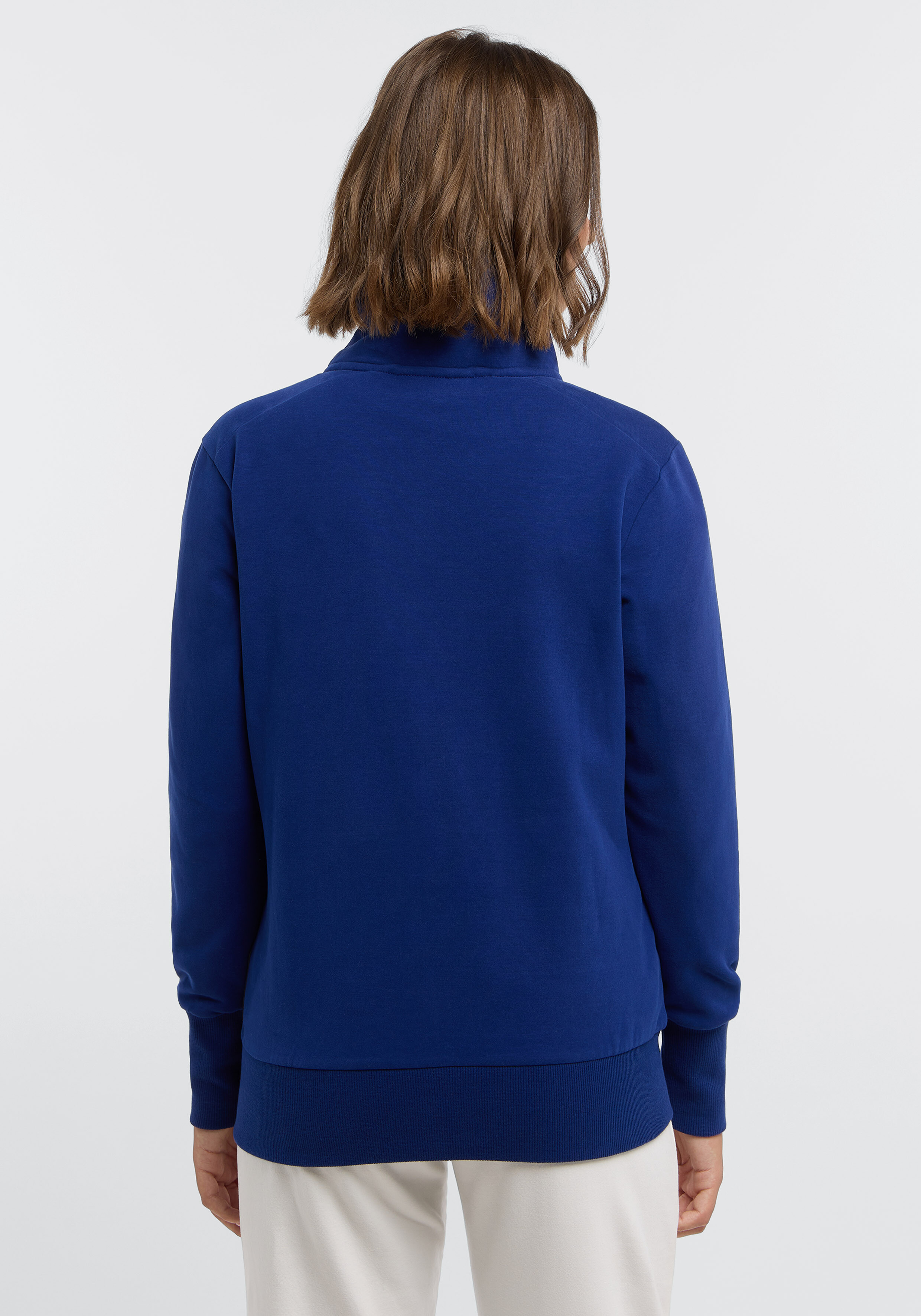Rückansicht einer Frau, die ein gemütliches königsblaues Sweatshirt mit Reißverschluss zum lässigen Faulenzen trägt.