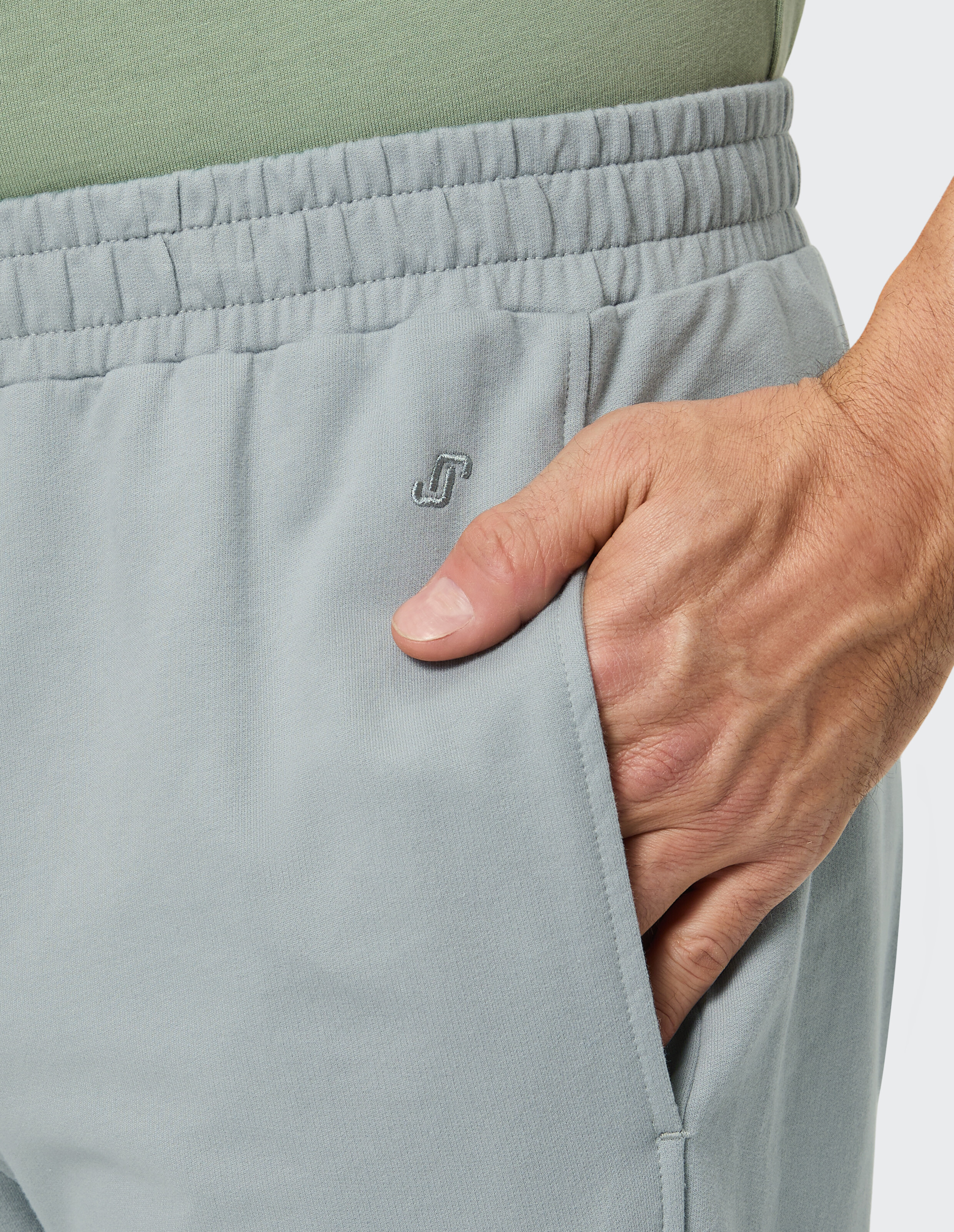 Eine graue Hose mit einem gestickten grauen Logo auf dem linken Oberschenkel und einem elastischen Bund mit sichtbaren Nähten.