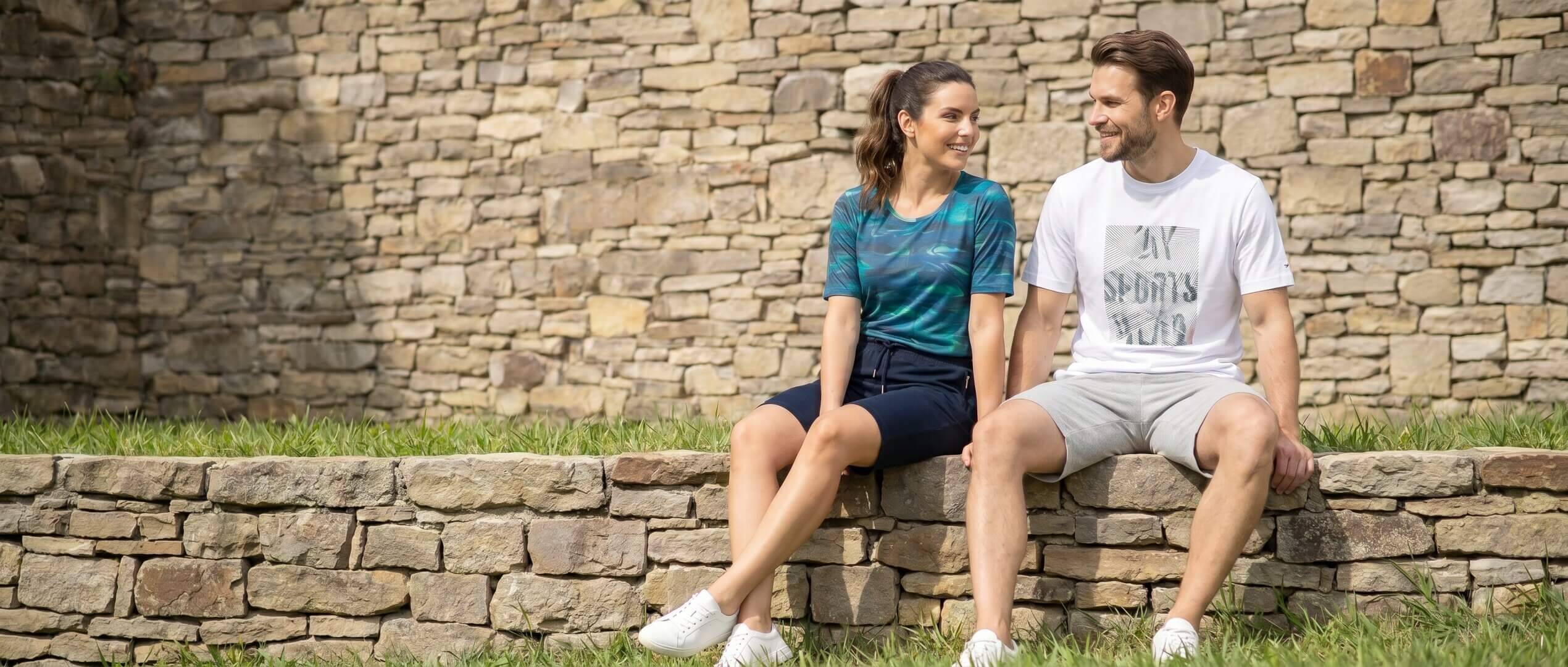 Paar in Freizeitkleidung, mit blau gemustertem Oberteil und weißem Grafik-T-Shirt, sitzt draußen.