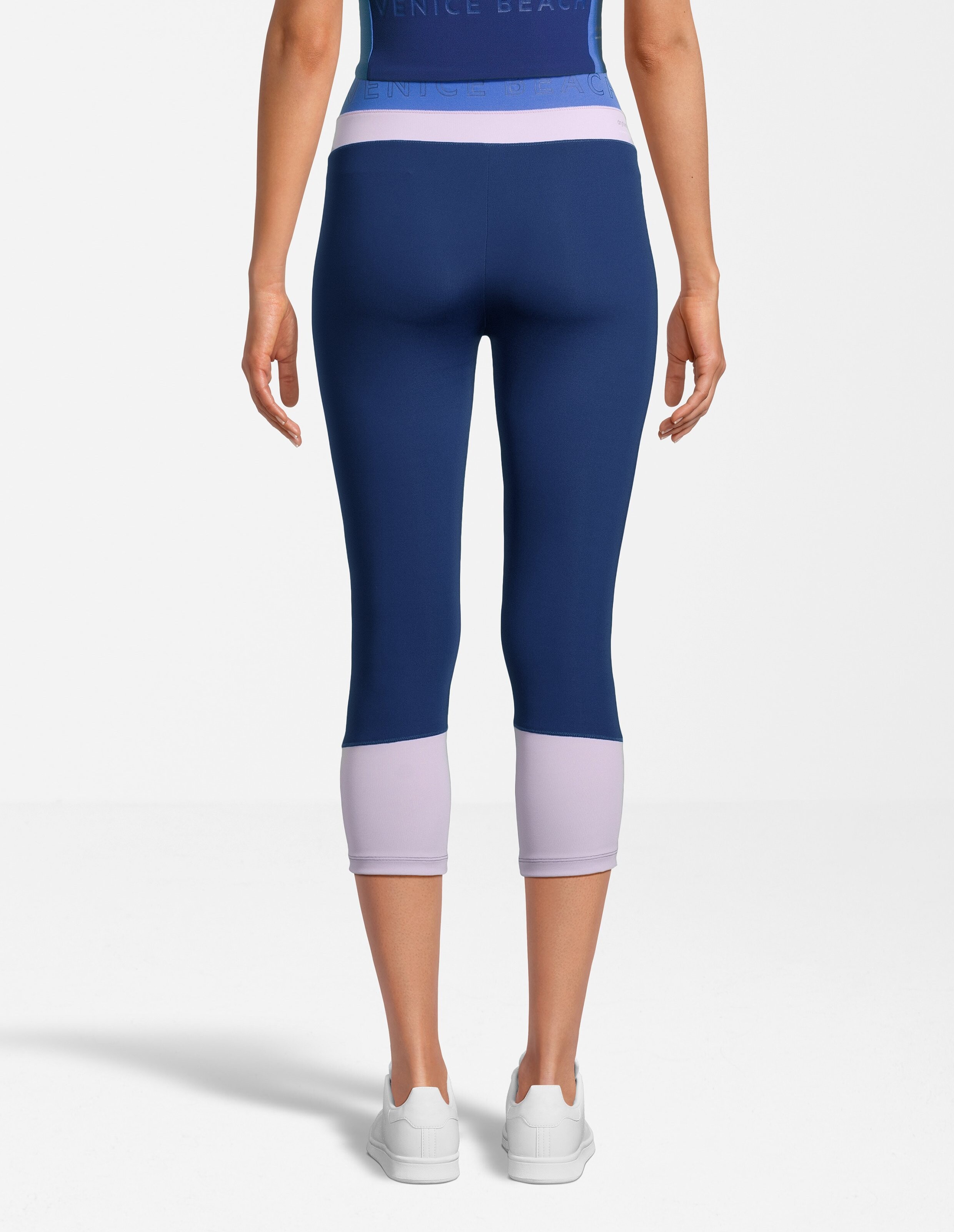 Rückansicht einer Frau in dunkelblauen und lavendelfarbenen Capri-Leggings, perfekt für Freizeitkleidung.