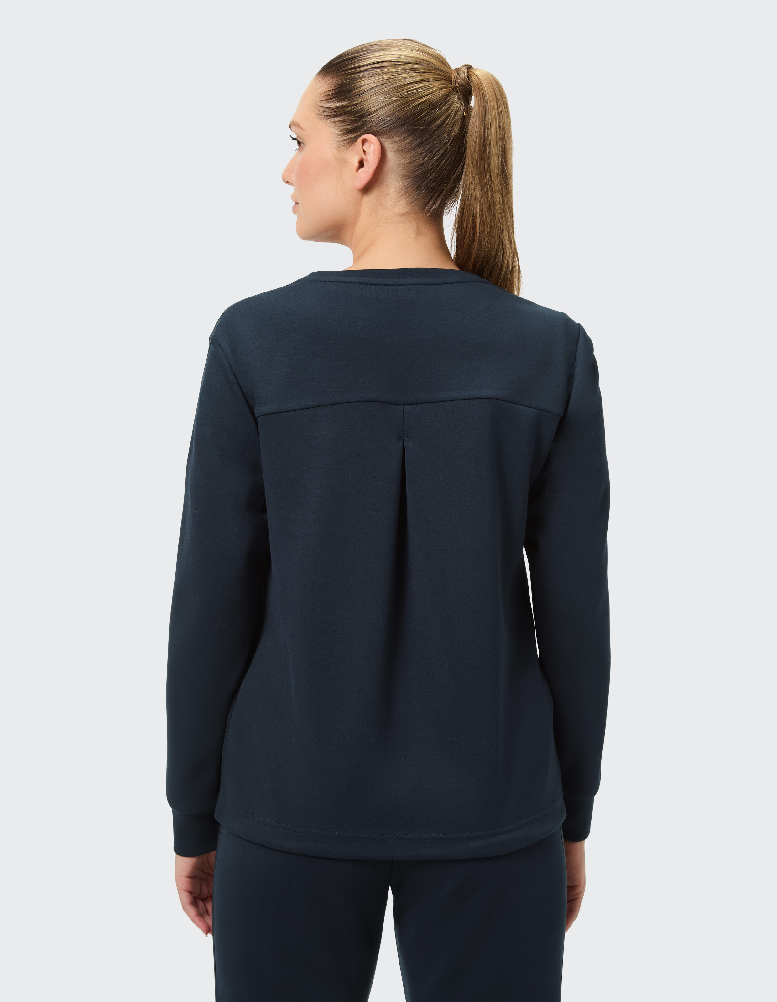 Rückansicht einer Frau in einem dunkelblauen, lässigen Sweatshirt mit Faltendetail, perfekt zum gemütlichen, stilvollen Faulenzen.