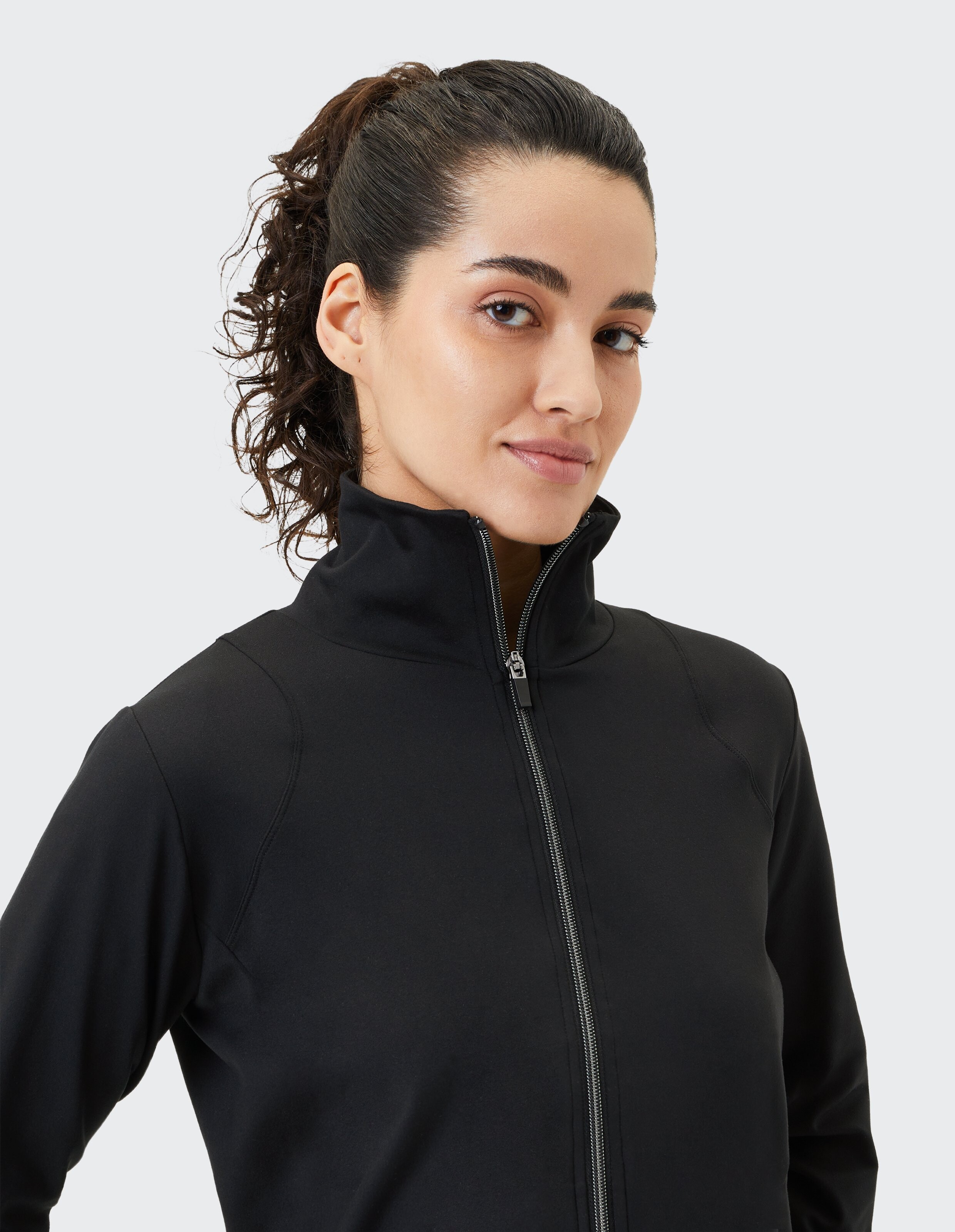 Frau in einer schwarzen Jacke mit Reißverschluss und hohem Kragen, die einen lässigen Stil zeigt.