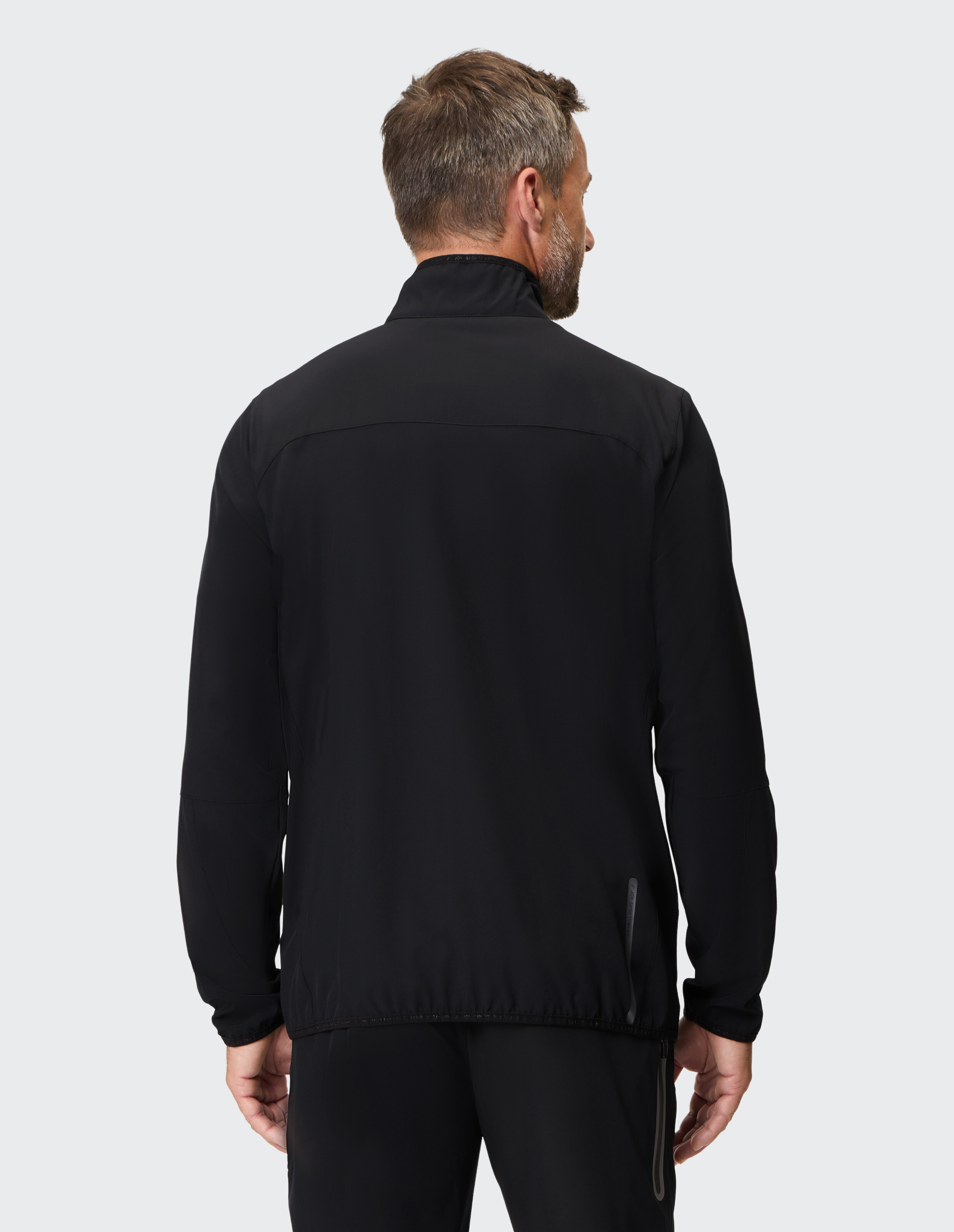 Mann trägt eine schwarze Freizeitjacke mit Reißverschluss, Rückansicht, ideal für Reisen oder Outdoor-Kleidung.