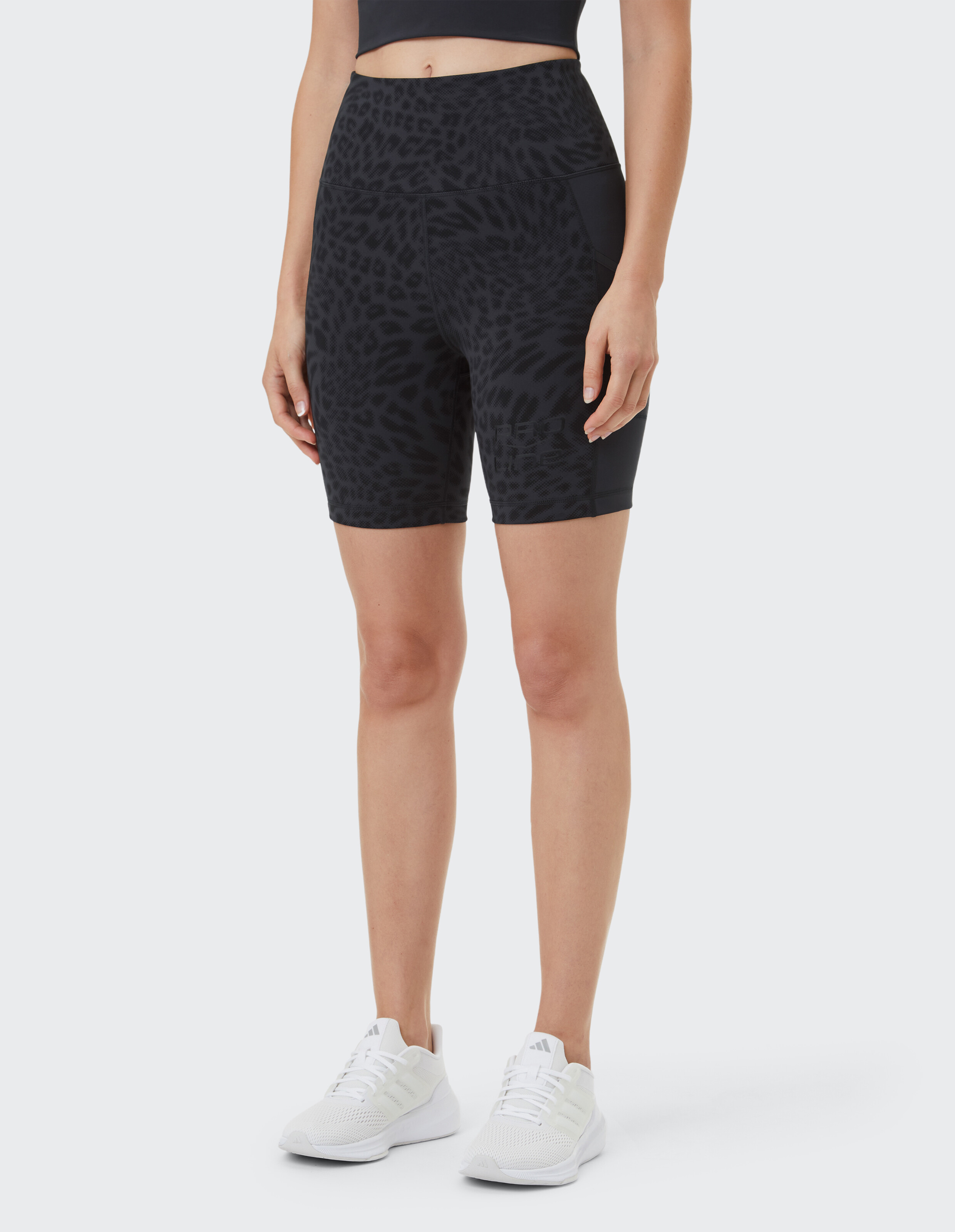 Frau trägt schwarze, hoch taillierte Bikershorts mit Leopardenmuster für einen lässigen, sportlichen Stil.