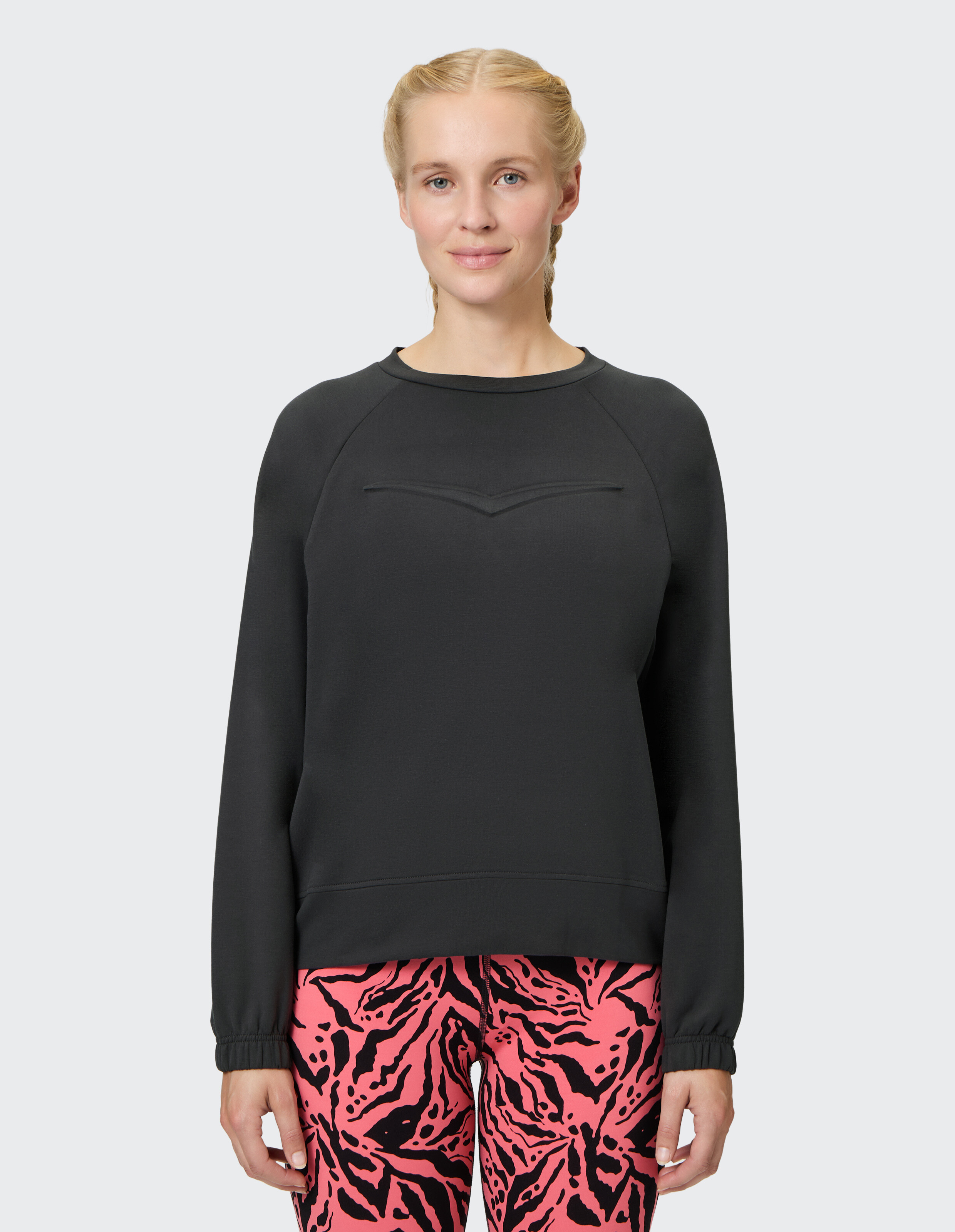 Frau trägt ein kuscheliges schwarzes Langarm-Sweatshirt und rosa Leggings mit Animal-Print.