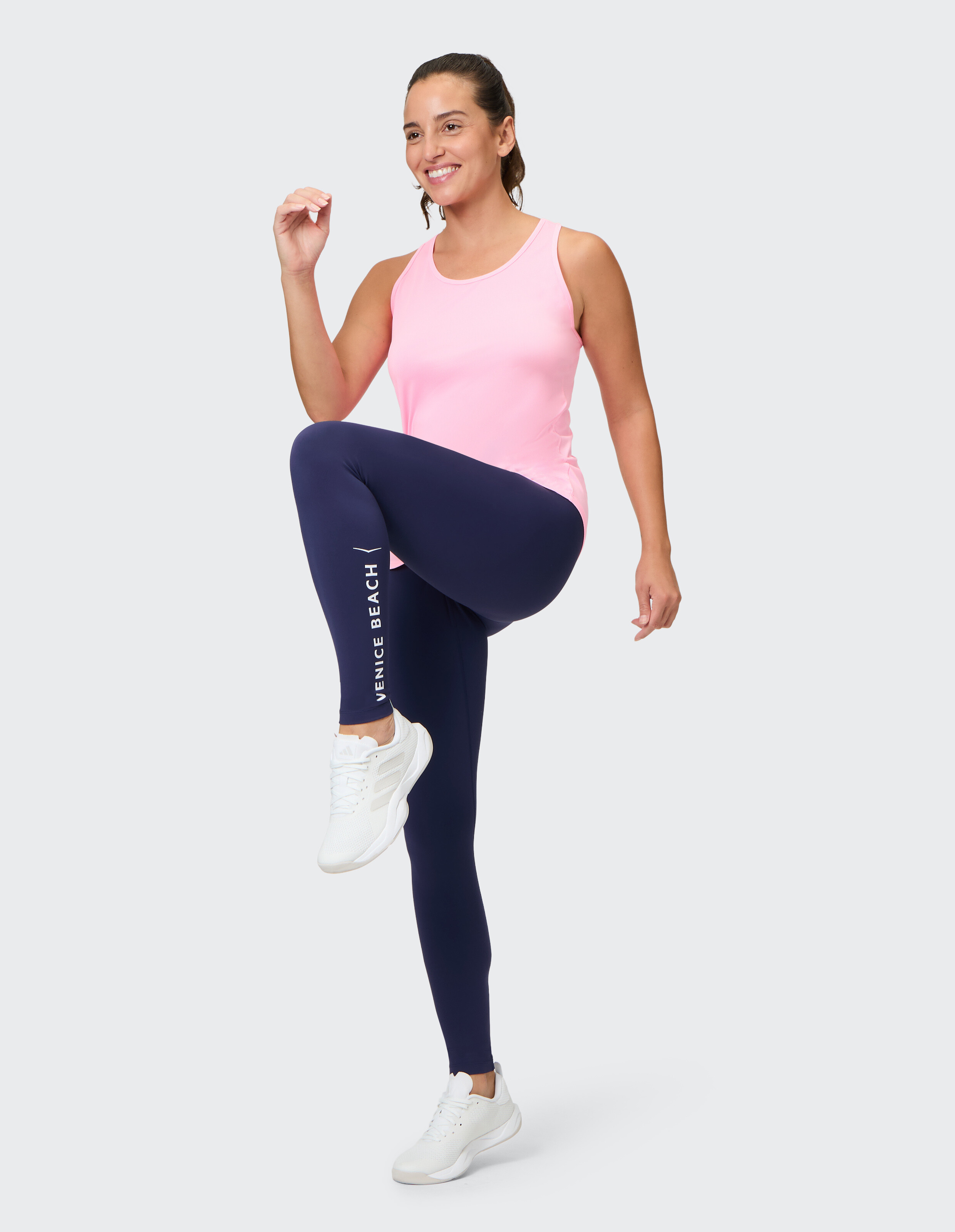 Frau in einem rosa Tanktop und dunkelblauen Leggings, die einen lässigen Activewear-Stil präsentiert.