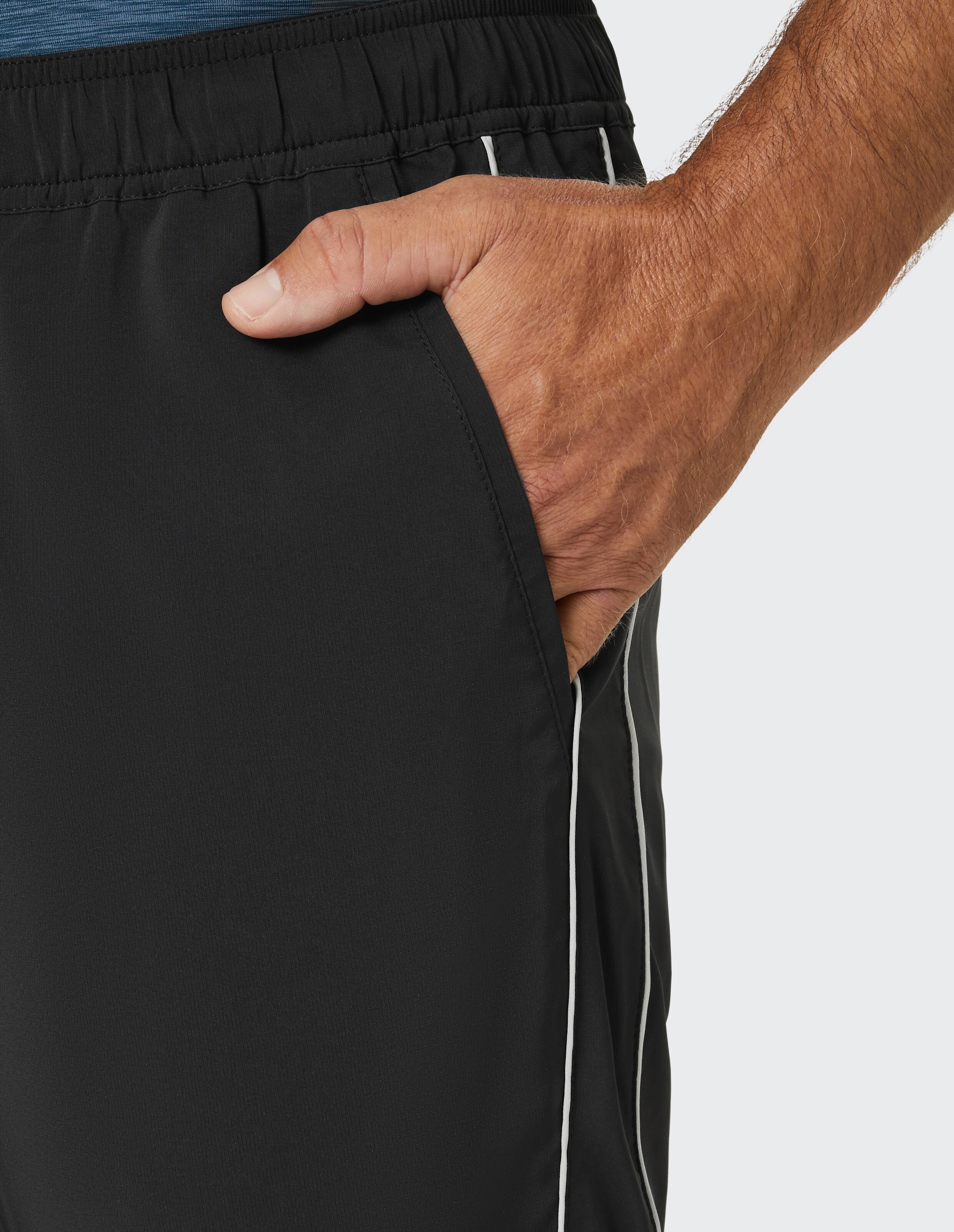 Eine Hand steckt lässig in der Seitentasche einer schwarzen Jogginghose mit weißen Streifen, getragen von einer Person.