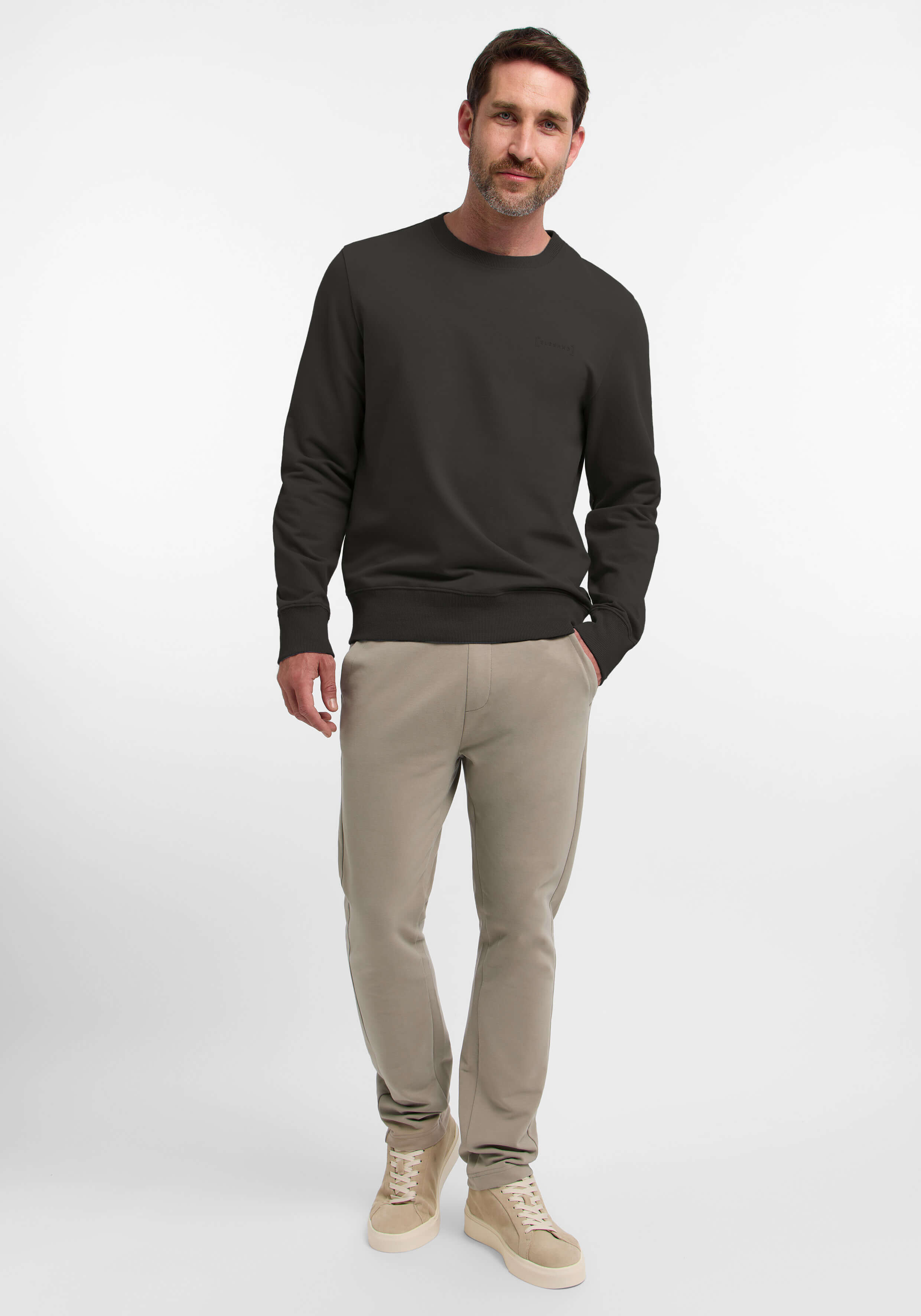 Mann trägt ein dunkelbraunes Sweatshirt mit Rundhalsausschnitt und eine beige Freizeithose.