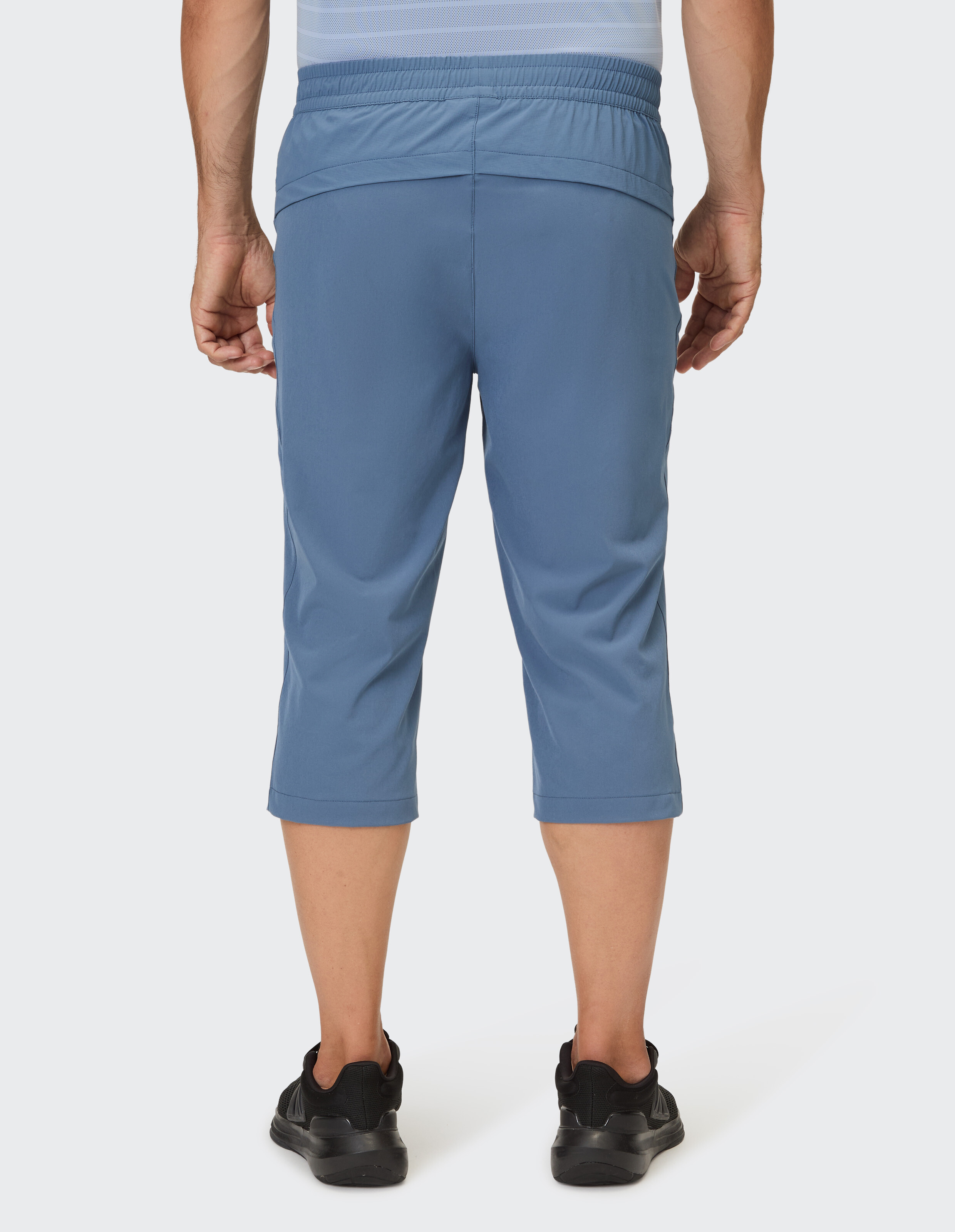 Mann trägt blaue 3/4-Sporthosen mit elastischem Bund und schwarzen Sneakers.