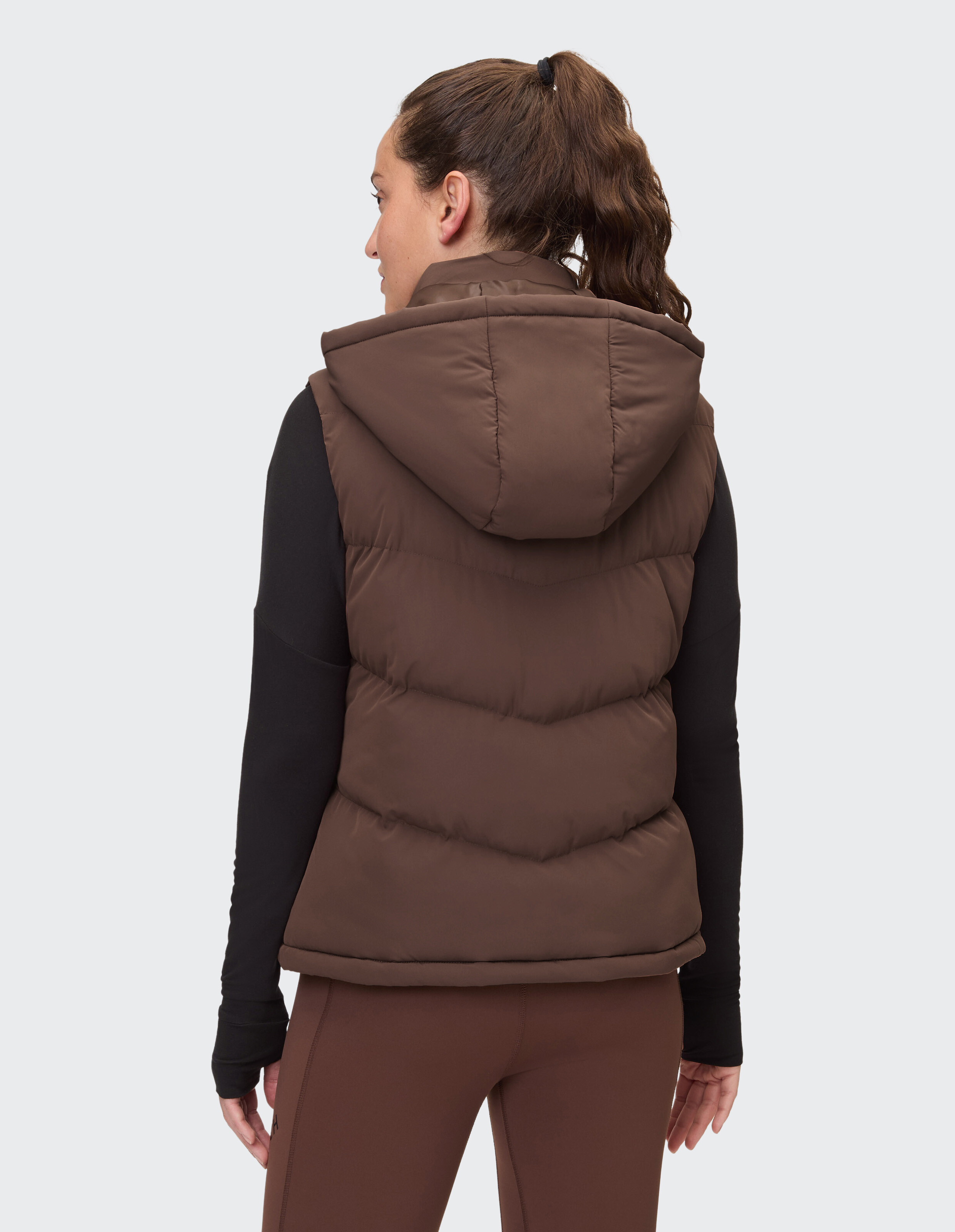 Frau trägt eine braune Steppweste mit Kapuze über einem schwarzen Langarmshirt.