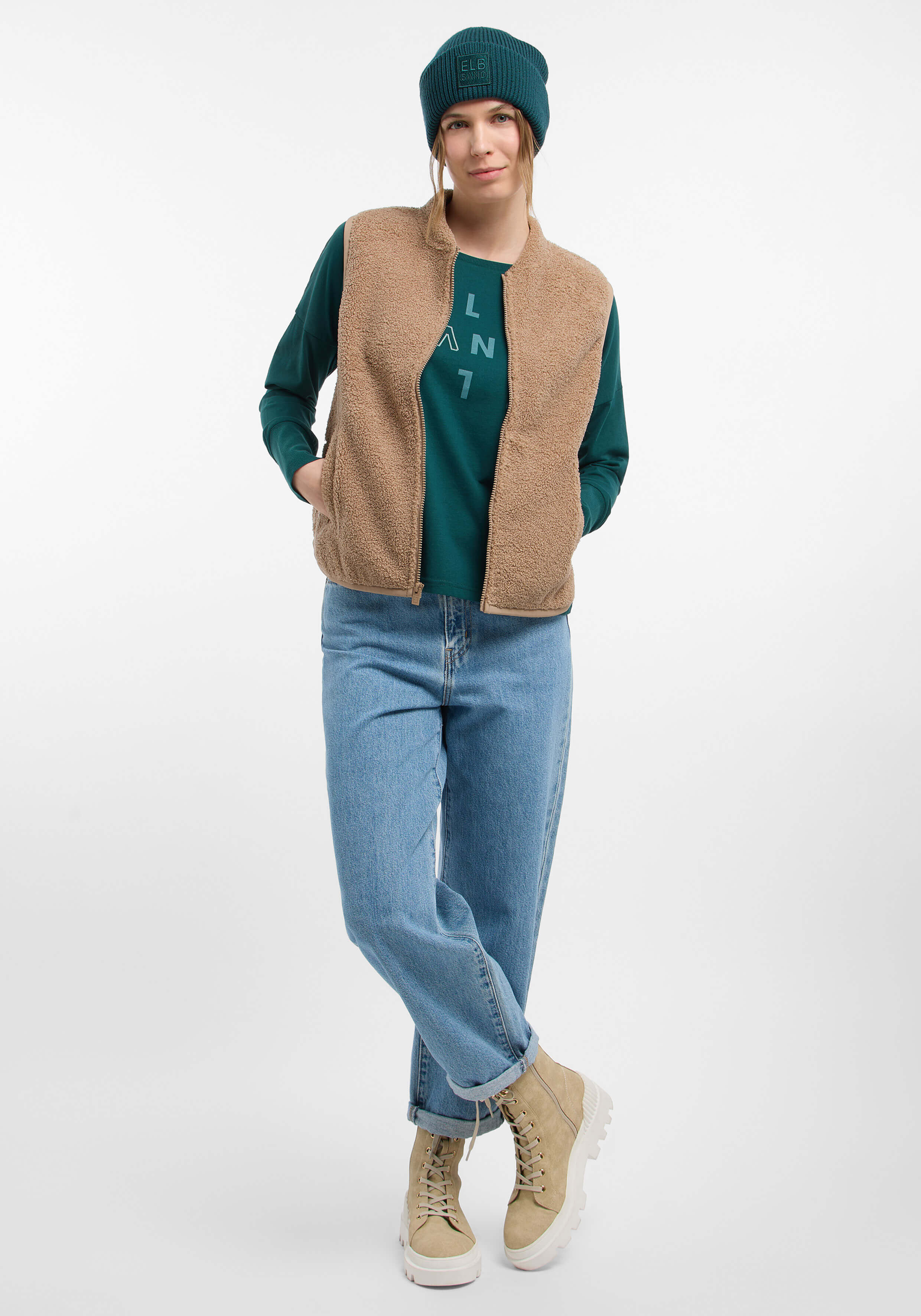 Frau trägt eine kuschelige beige Fleeceweste, ein grünes Langarmhemd und eine Mütze.