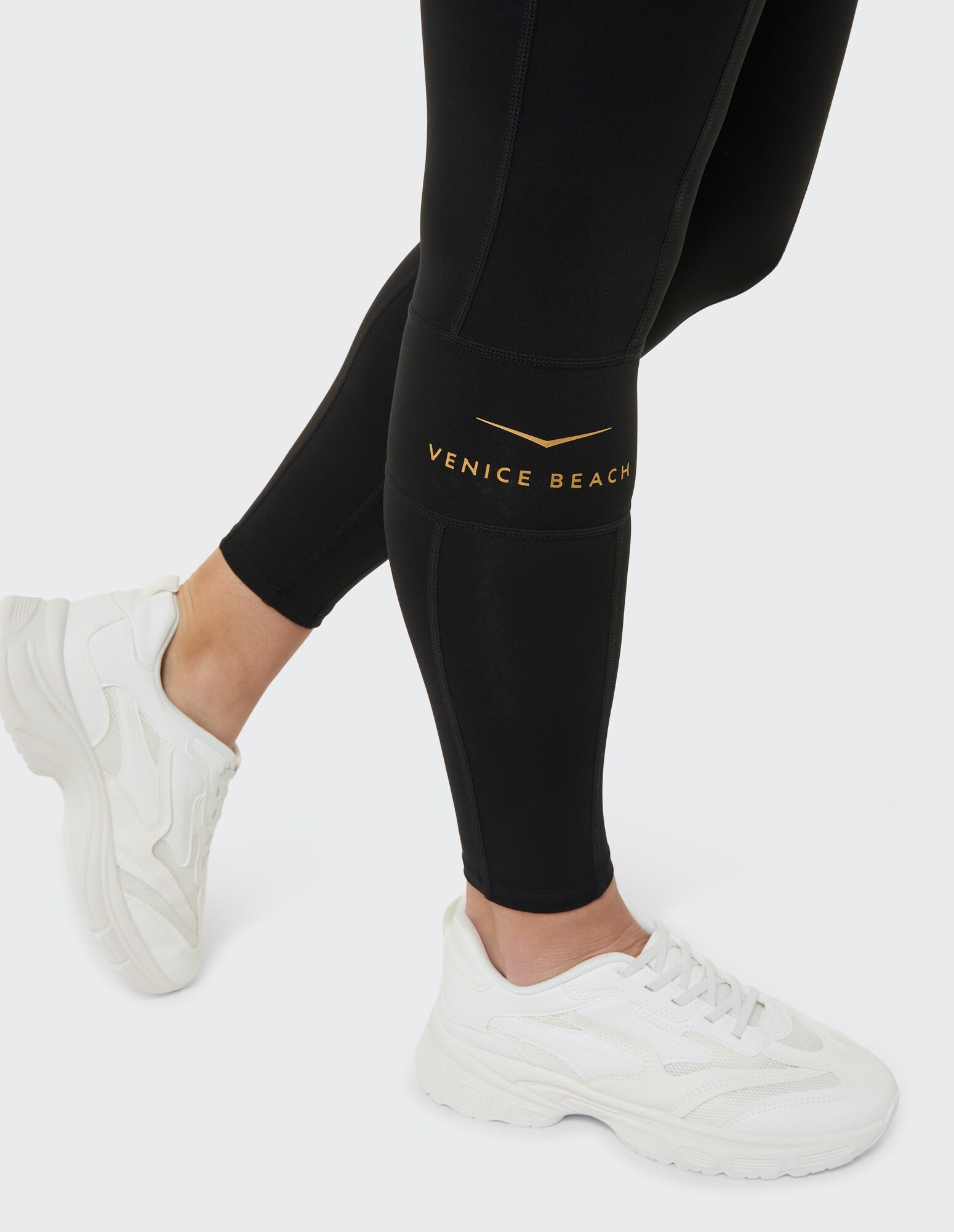 Schwarze Leggings mit „Venice Beach“-Logo, gepaart mit weißen Sneakers für Freizeitkleidung.