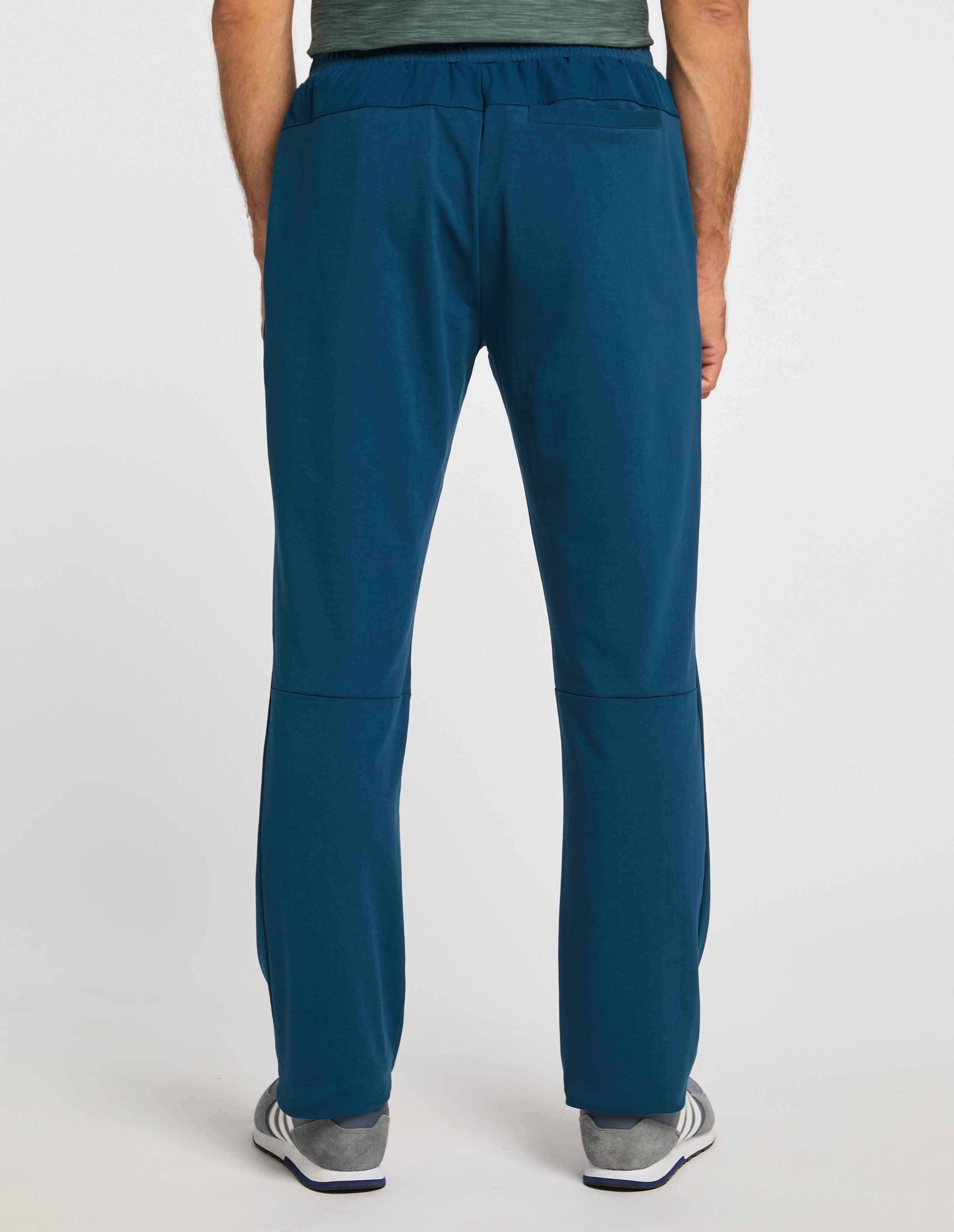 Person in blauer Jogginghose und graugrünen T-Shirt von hinten, weiße Turnschuhe mit grauen Details auf hellem Hintergrund.