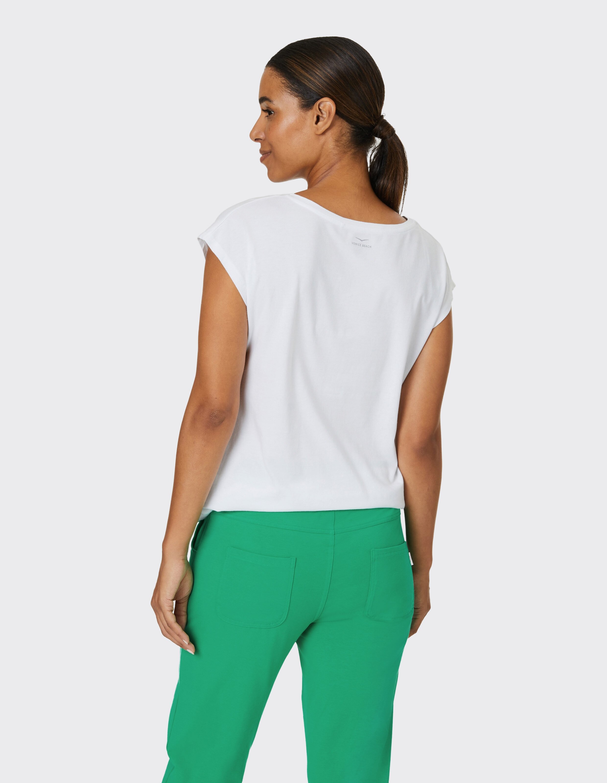 Frau trägt ein weißes Freizeit-T-Shirt und eine grüne Hose für einen bequemen Lounge-Look.
